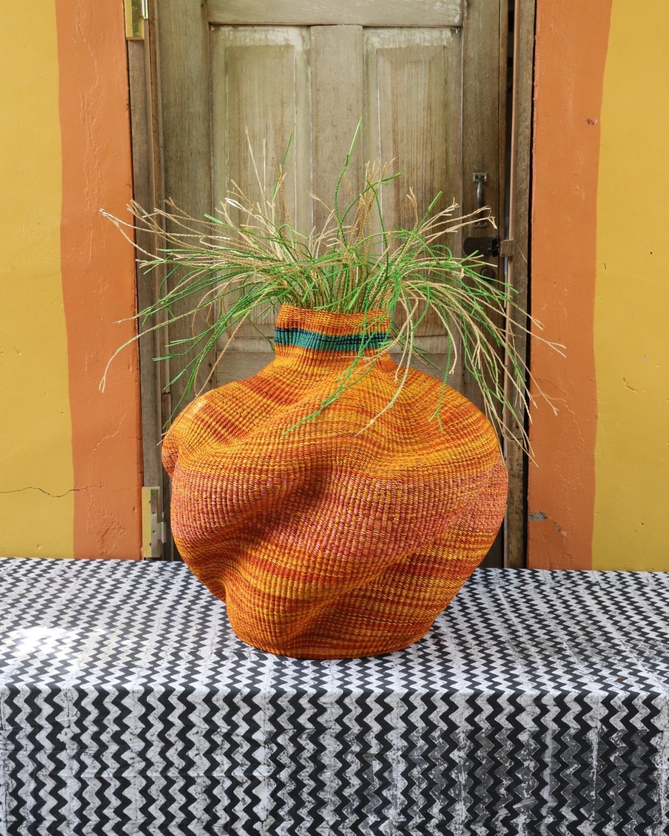 A colorful, handwoven piece sitting on a black and white cloth with decorative straw branching out.