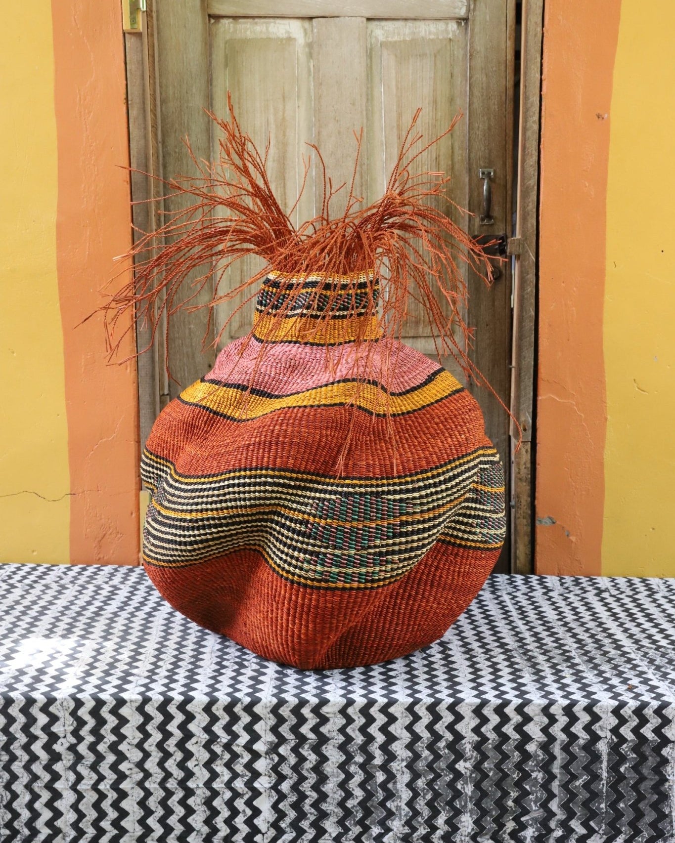 A colorful, handwoven piece sitting on a black and white cloth with decorative straw branching out.