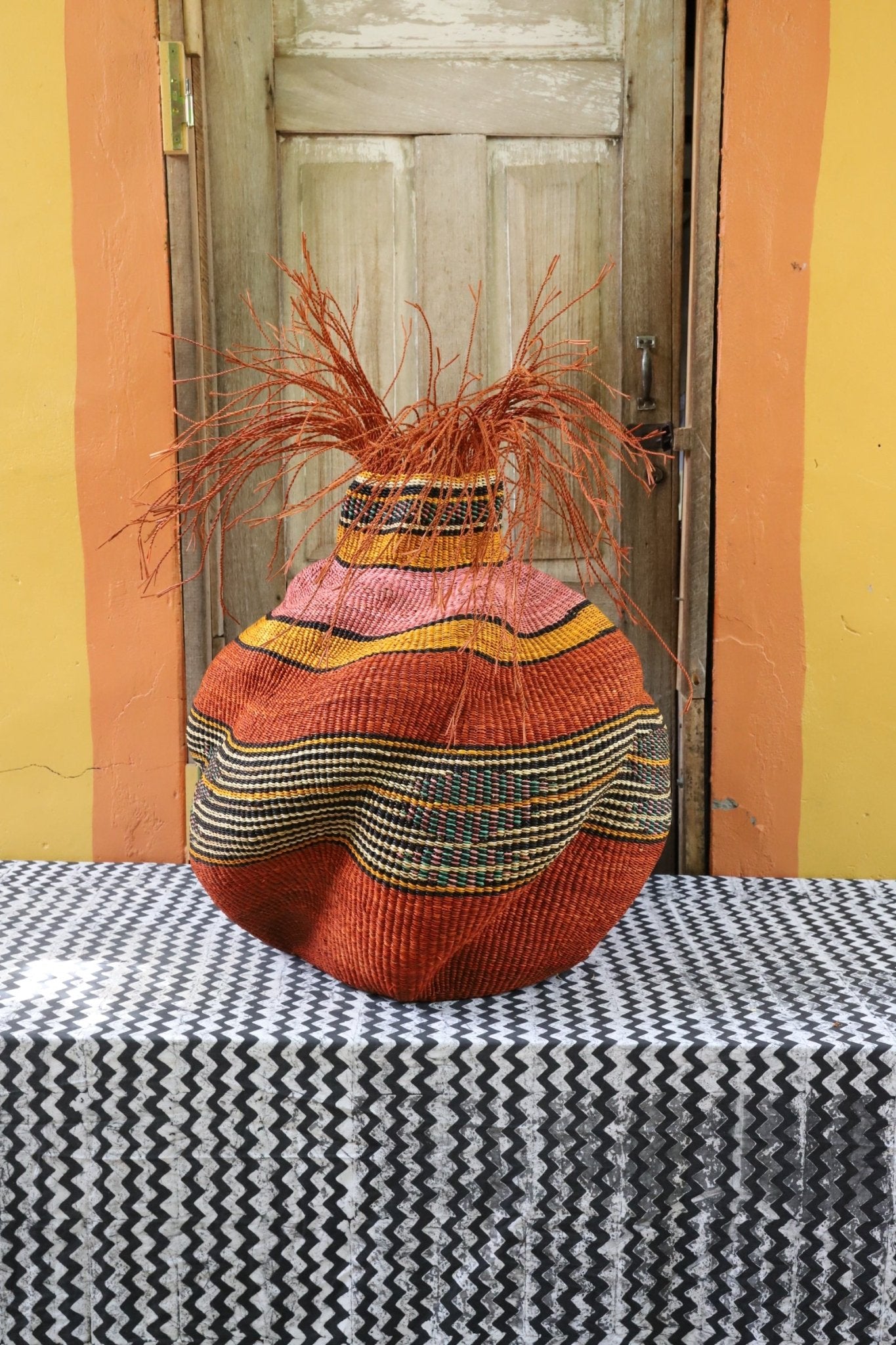 A colorful, handwoven piece sitting on a black and white cloth with decorative straw branching out.