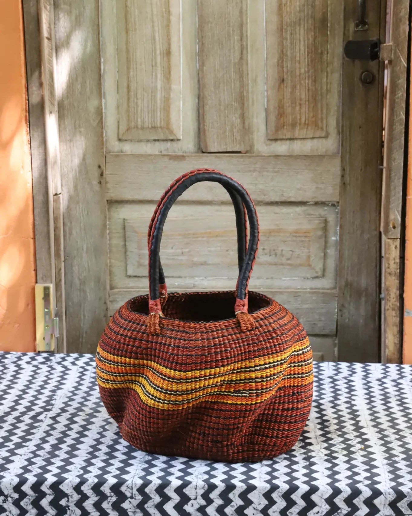 Woven carry on basket with premium leather on a black and white cloth against a wooden door