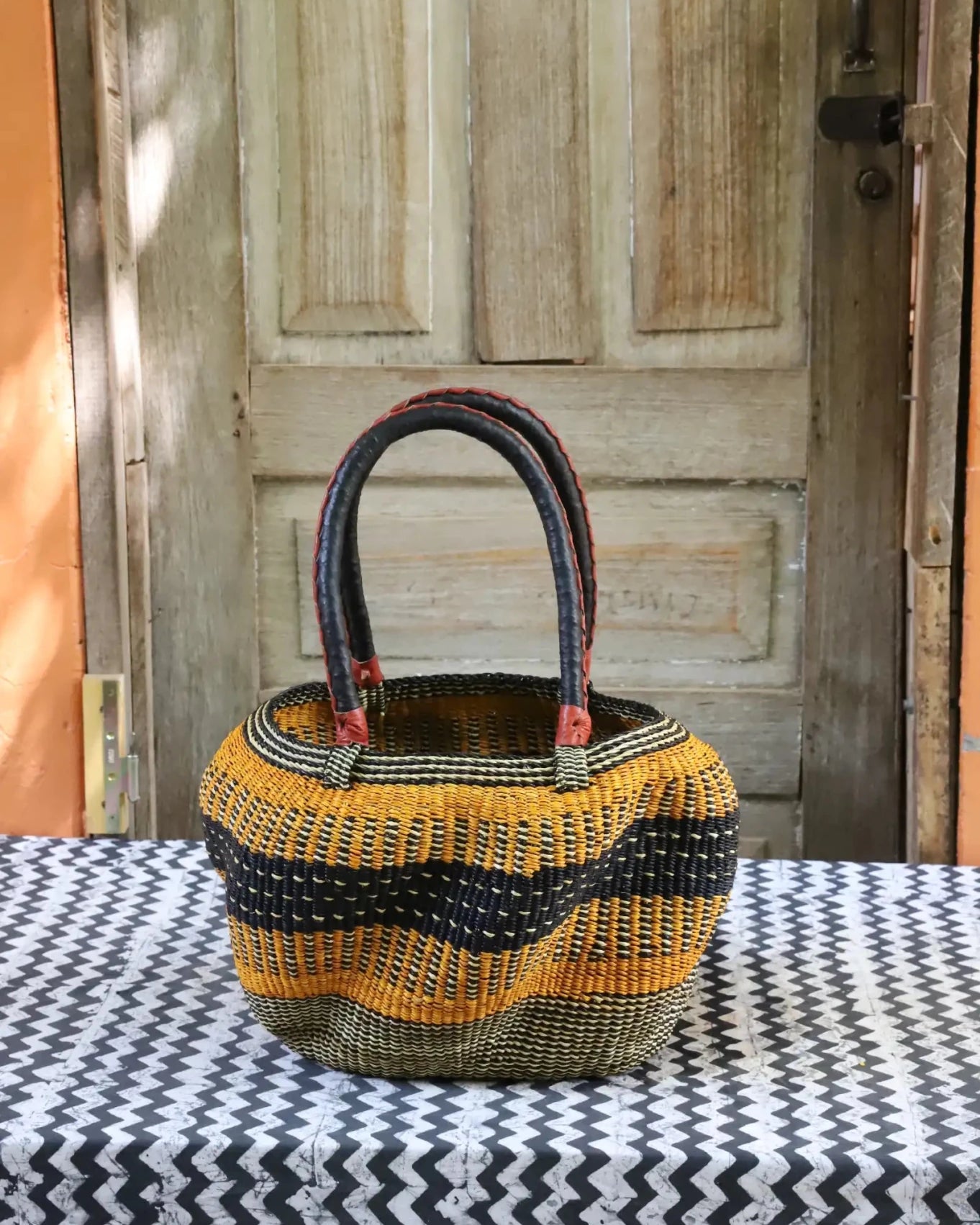 Woven carry on basket with premium leather on a black and white cloth against a wooden door
