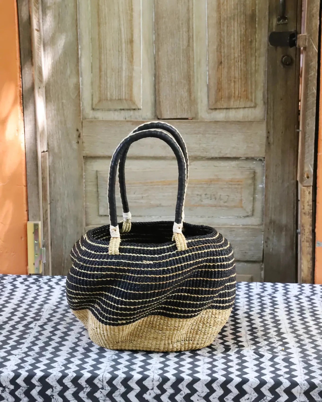 Woven carry on basket with premium leather on a black and white cloth against a wooden door