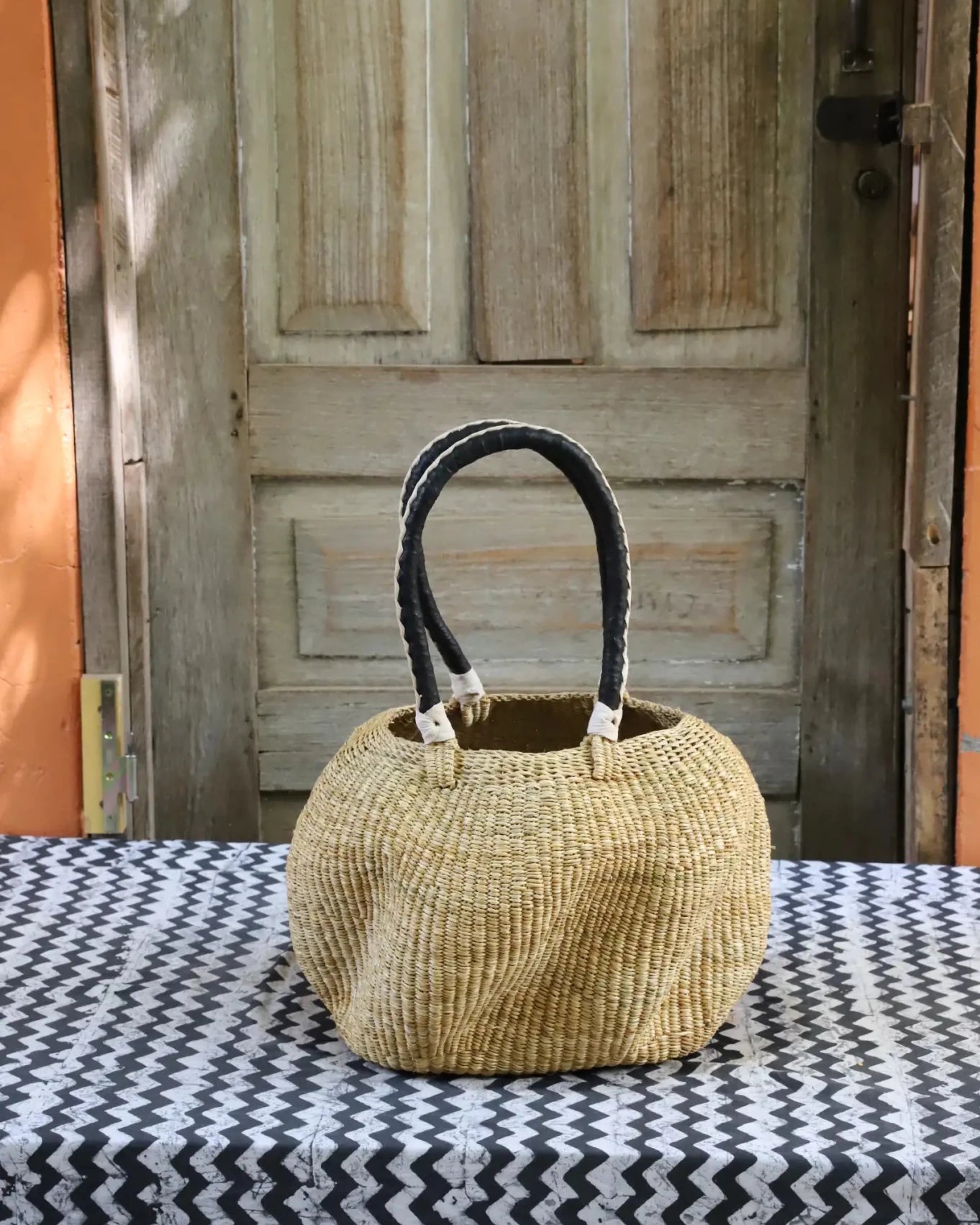 Woven carry on basket with premium leather on a black and white cloth against a wooden door