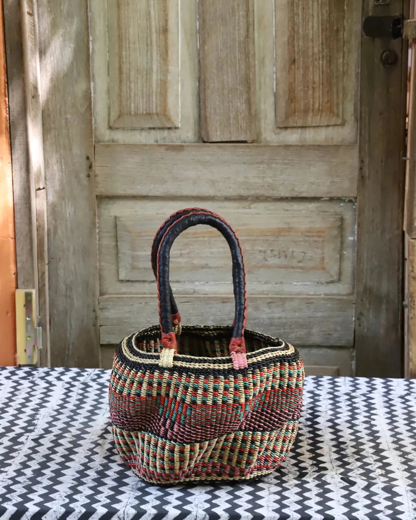 Woven carry on basket with premium leather on a black and white cloth against a wooden door