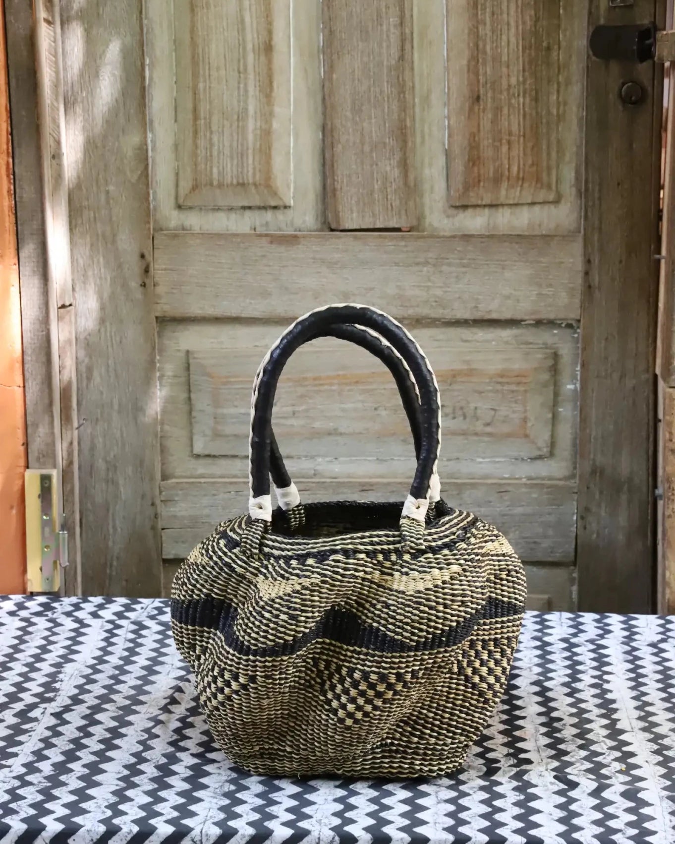 Woven carry on basket with premium leather on a black and white cloth against a wooden door