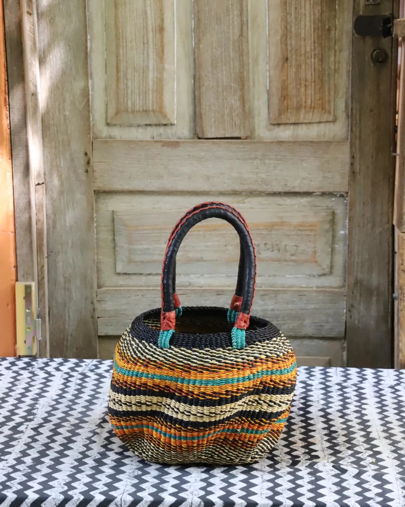 Woven carry on basket with premium leather on a black and white cloth against a wooden door
