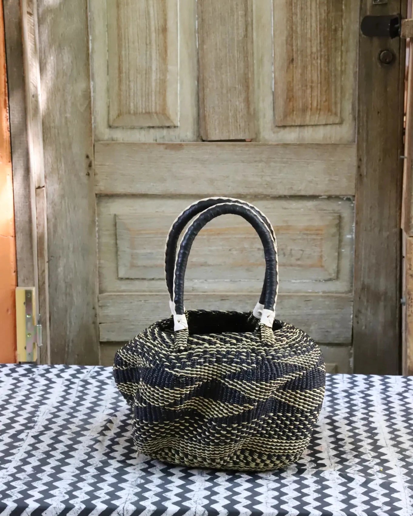 Woven carry on basket with premium leather on a black and white cloth against a wooden door
