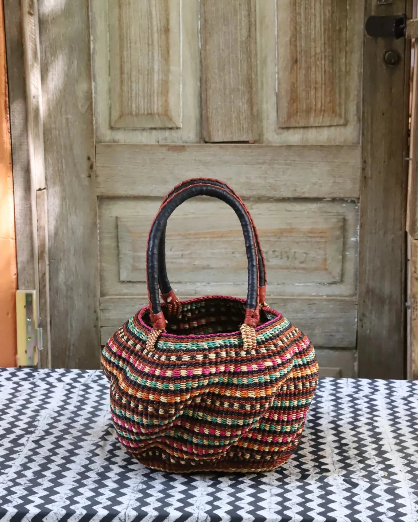 Woven carry on basket with premium leather on a black and white cloth against a wooden door