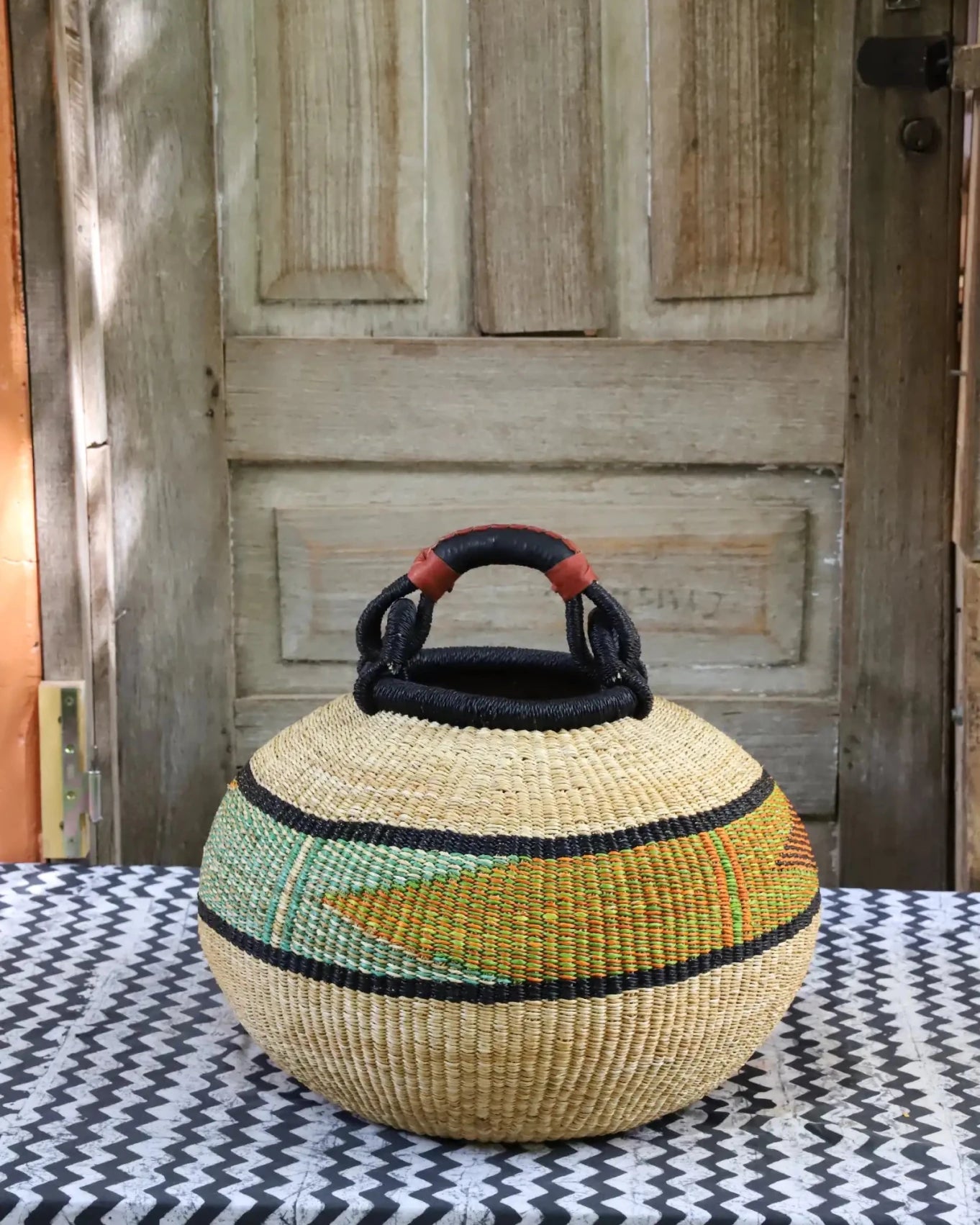 Colourful storage basket sitting on a black and white cloth against a wooden door.