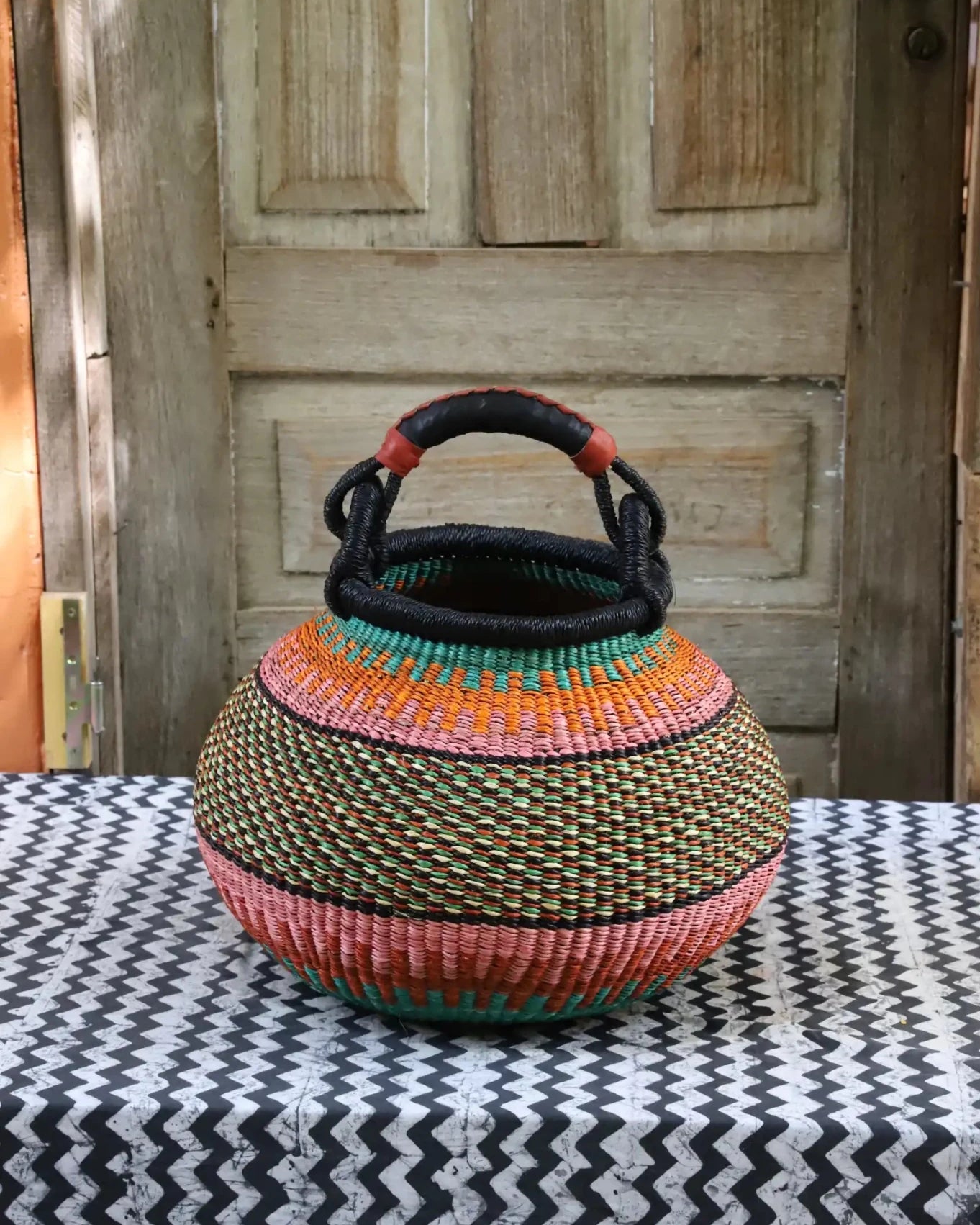 Colourful storage basket sitting on a black and white cloth against a wooden door.