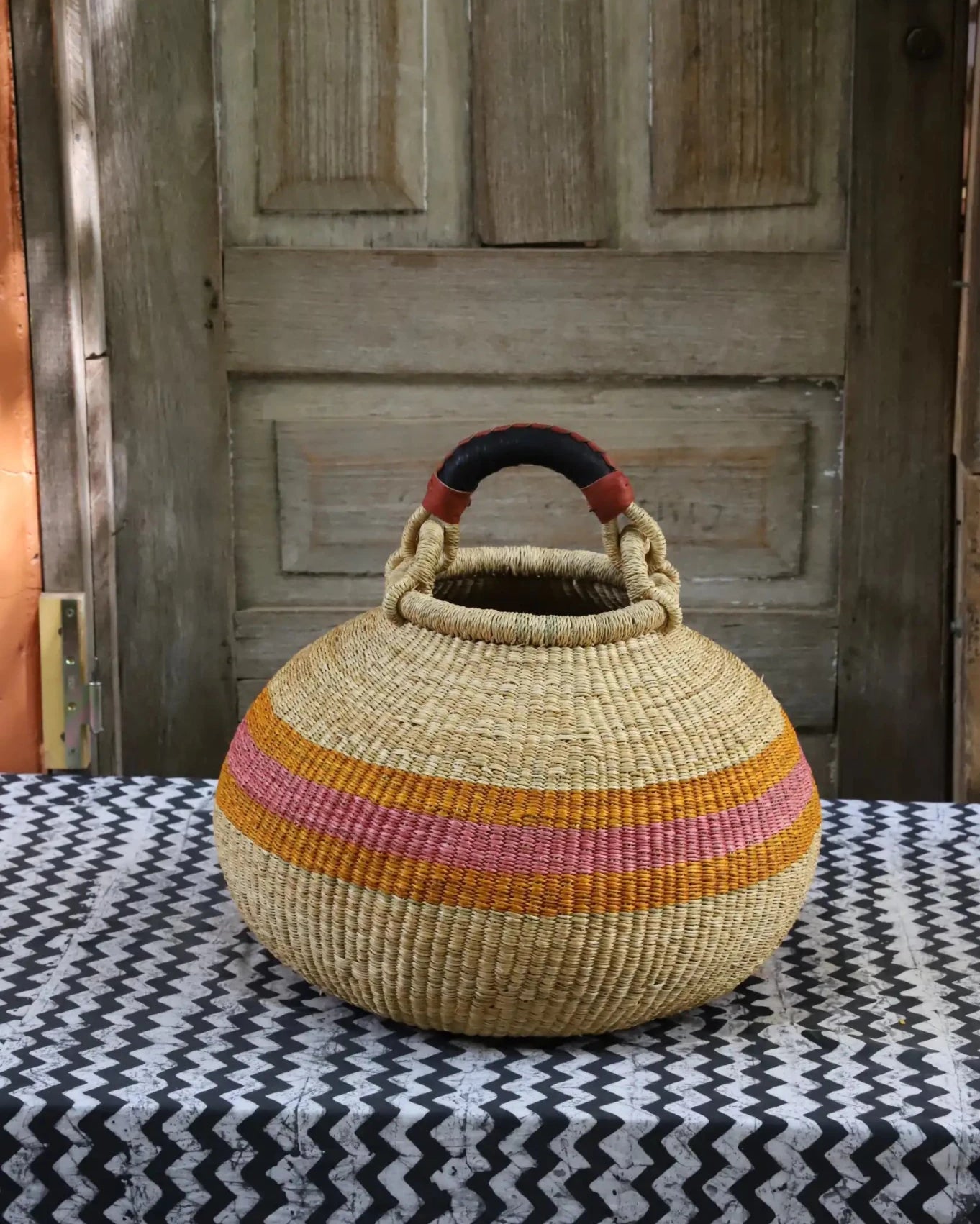 Colourful storage basket sitting on a black and white cloth against a wooden door.