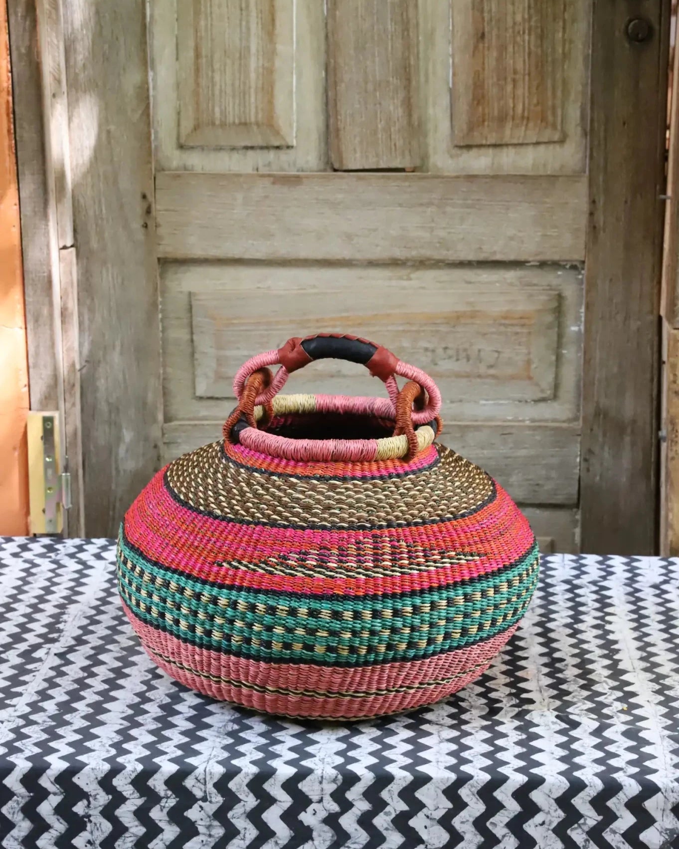 Colourful storage basket sitting on a black and white cloth against a wooden door.