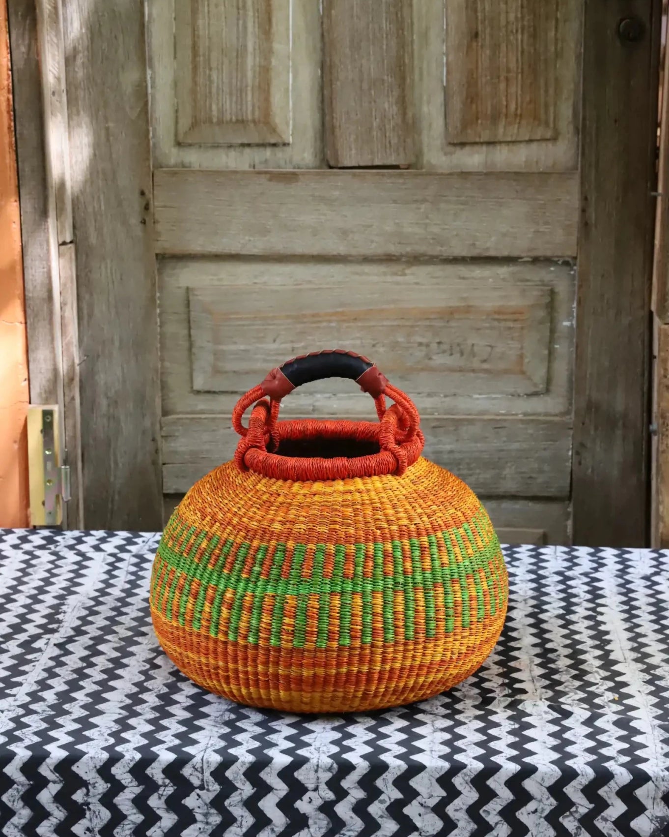 Colourful storage basket sitting on a black and white cloth against a wooden door.
