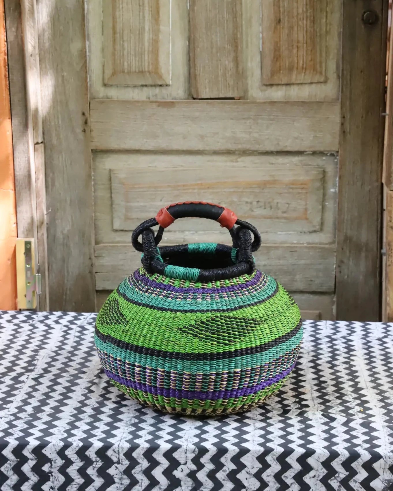 Colourful storage basket sitting on a black and white cloth against a wooden door.