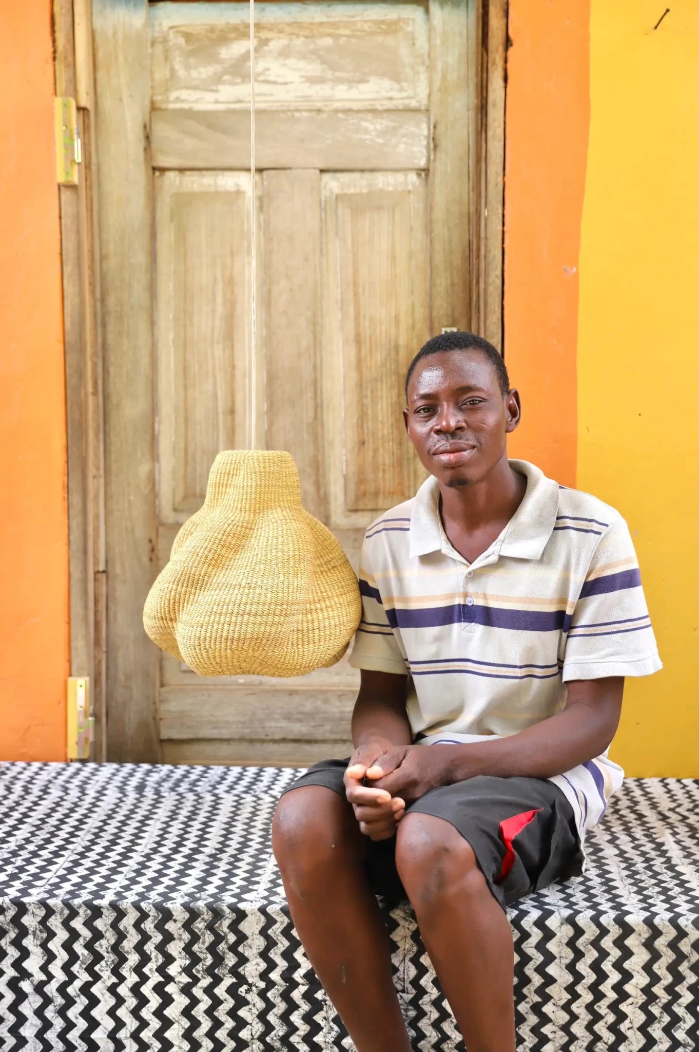 Man sitting on a bed with a woven basket in front of a colorful wall.