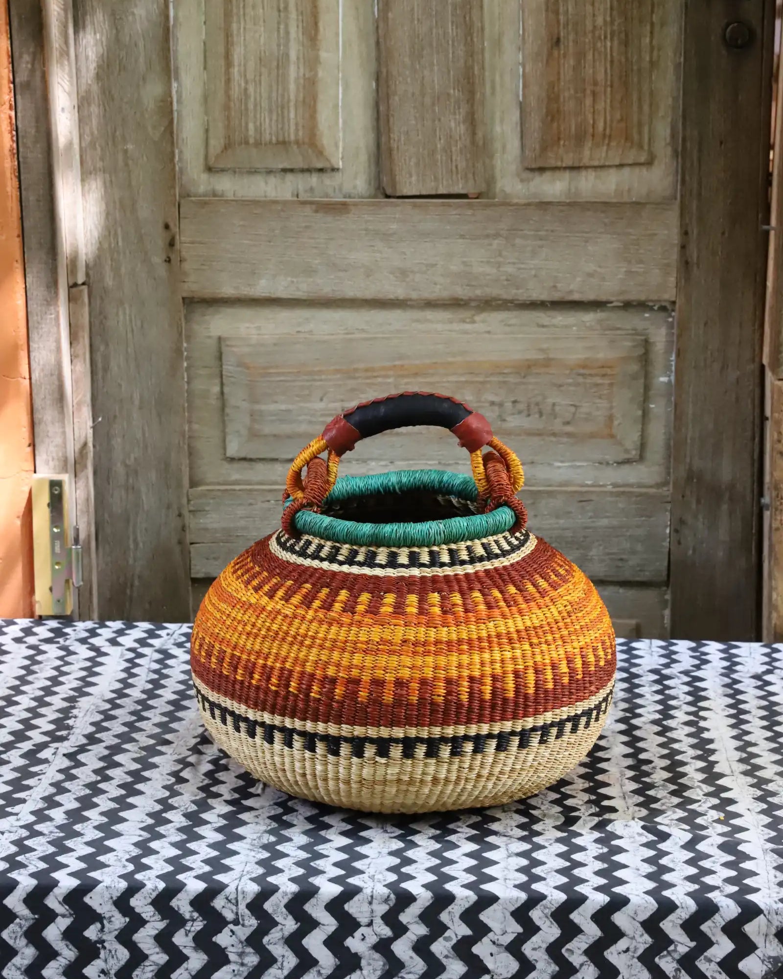 Colourful storage basket sitting on a black and white cloth against a wooden door.