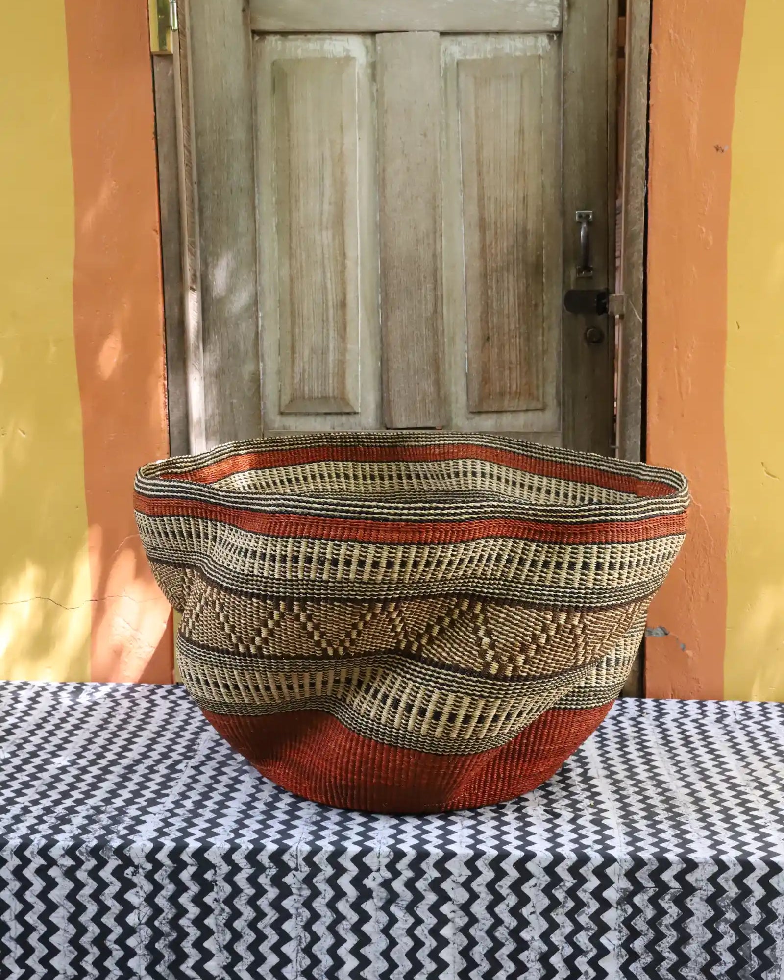 Woven basket with geometric pattern on a black and white checkered tablecloth in front of a wooden door.