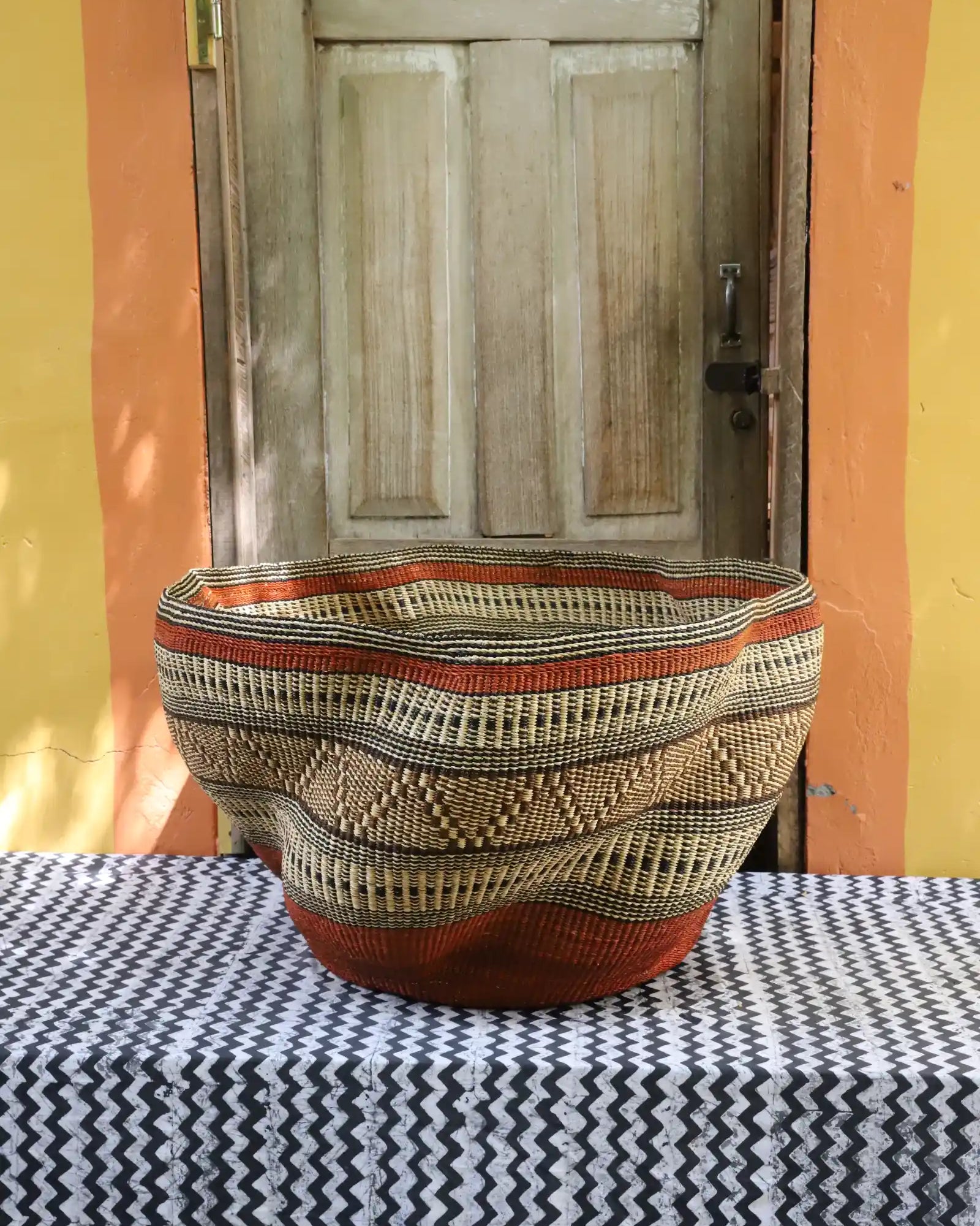 Woven basket with geometric pattern on a tablecloth in front of a wooden door.