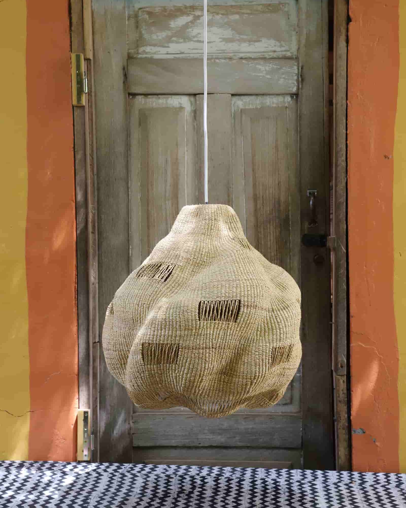 Textured pendant light hanging in front of a wooden door with a colorful wall.