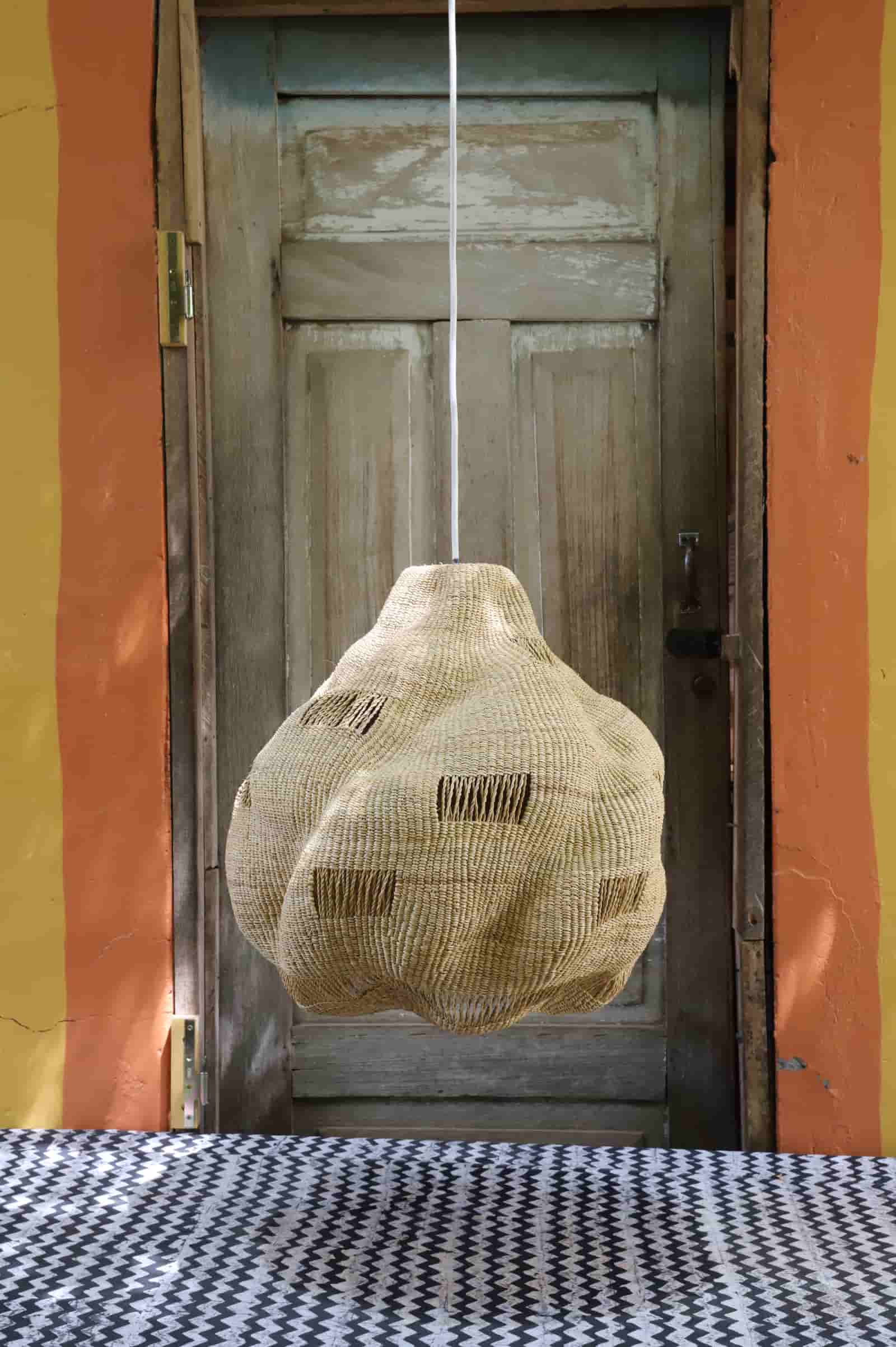 Textured pendant light hanging in front of a wooden door with a colorful wall.