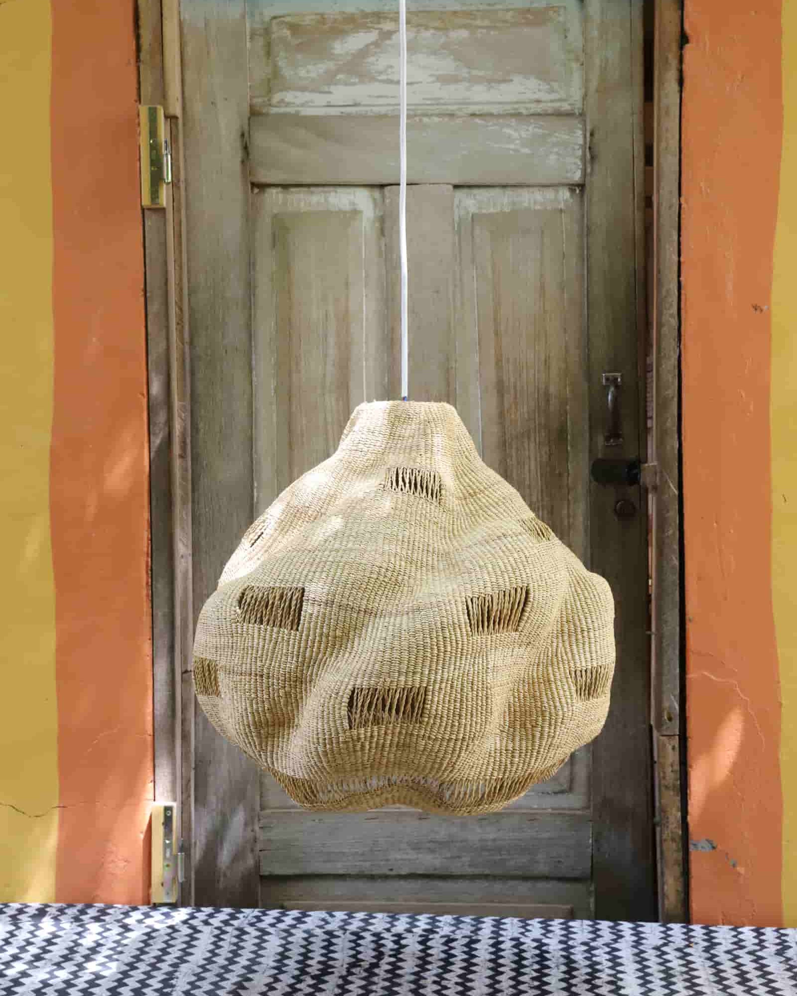 Textured bag hanging from a string in front of a wooden door with a colorful wall background.