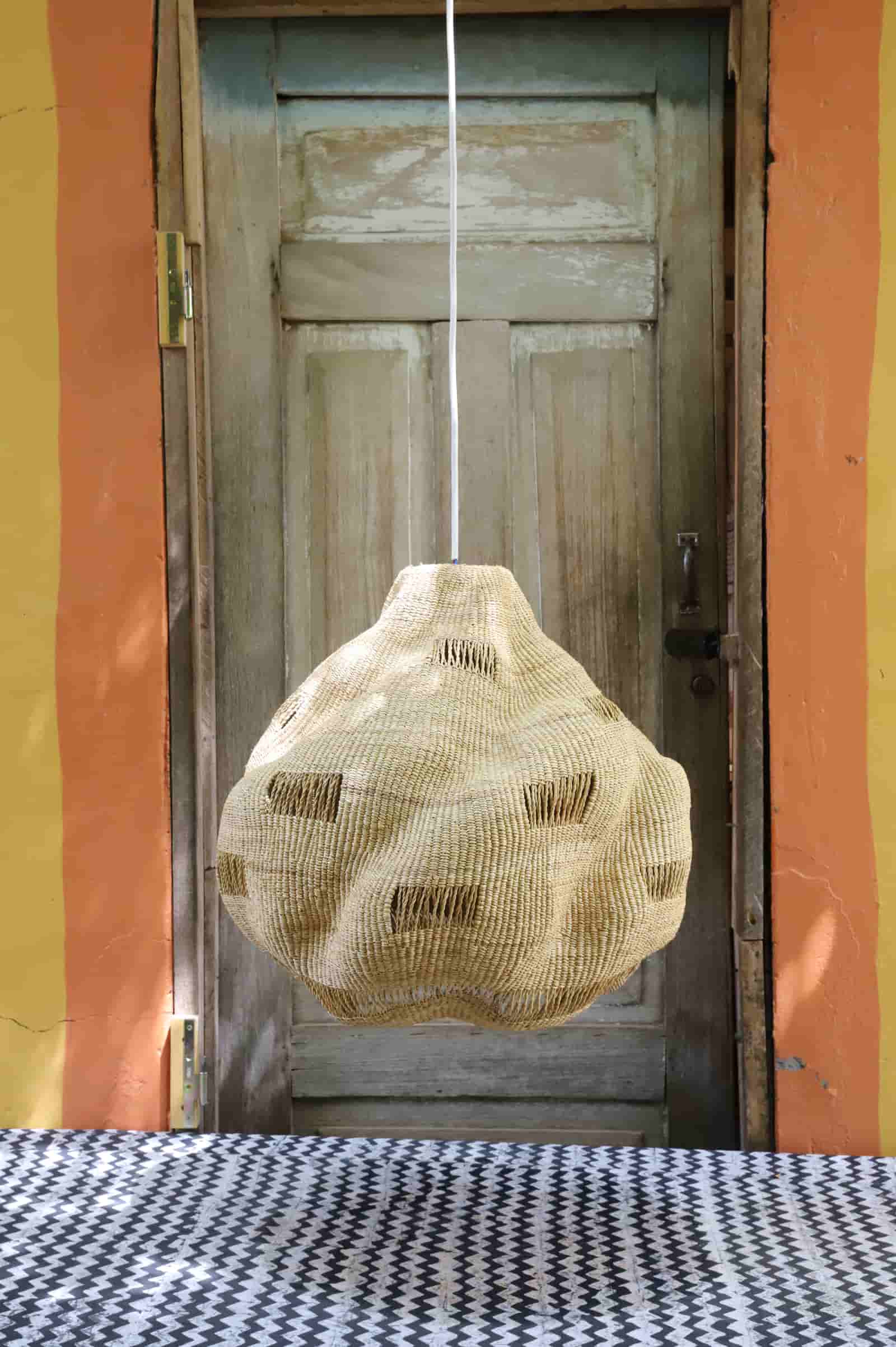 Textured bag hanging from a string in front of a wooden door with a colorful wall background.