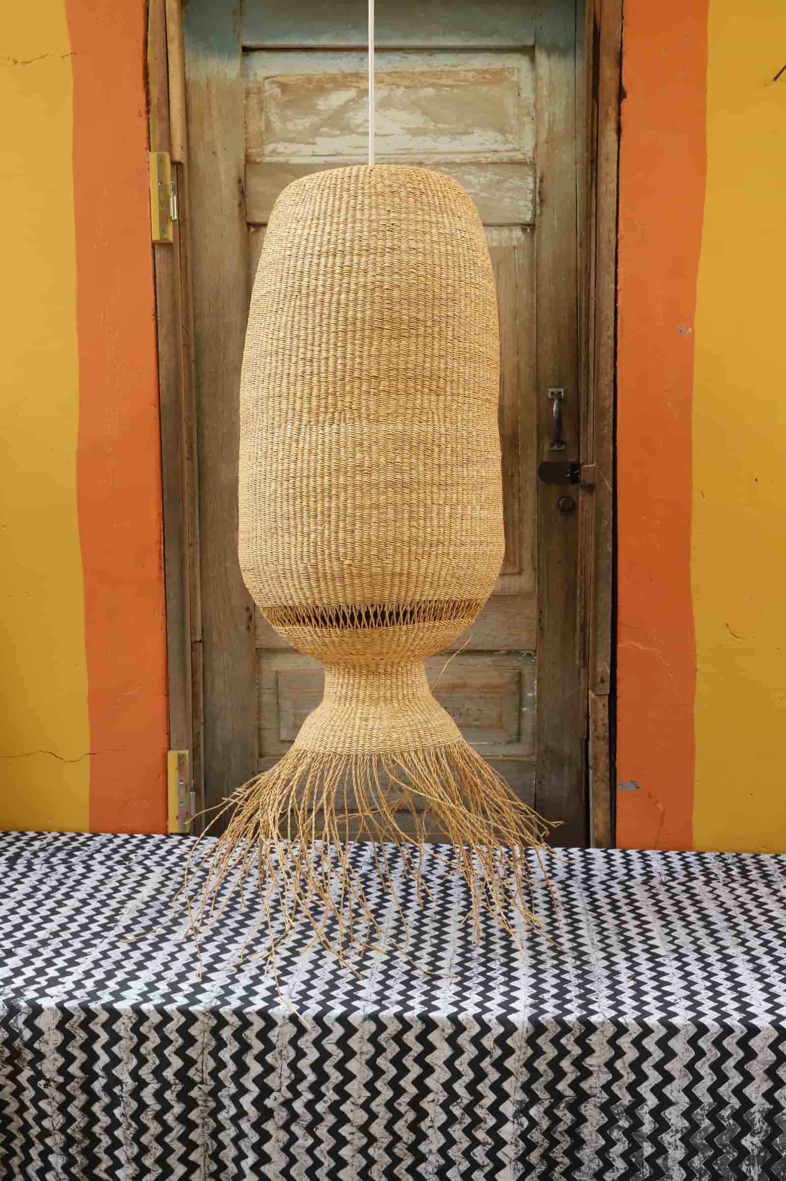 Woven lamp hanging above a table with a black and white patterned tablecloth against a yellow wall.