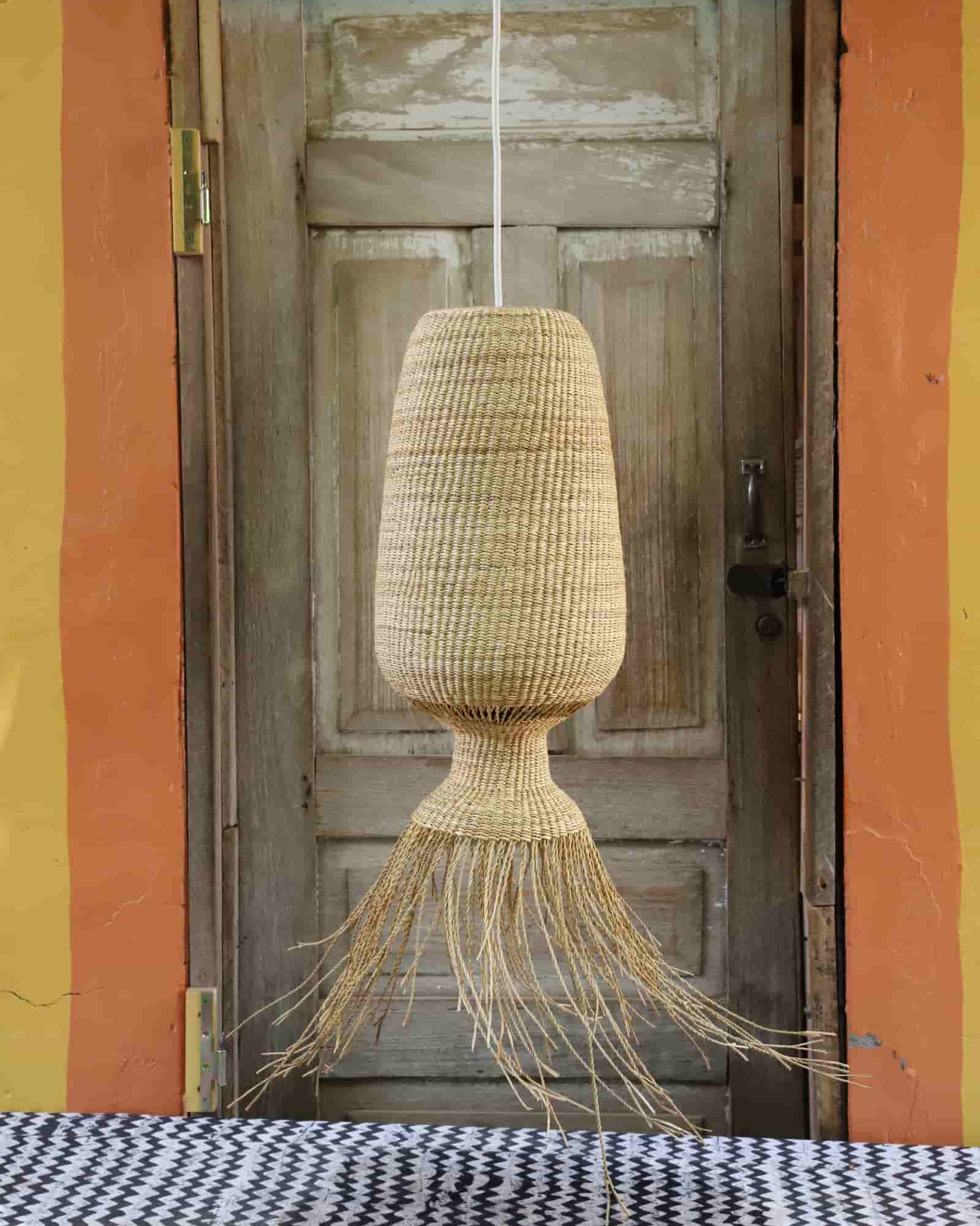 Woven pendant light hanging in front of a rustic wooden door with colorful walls.