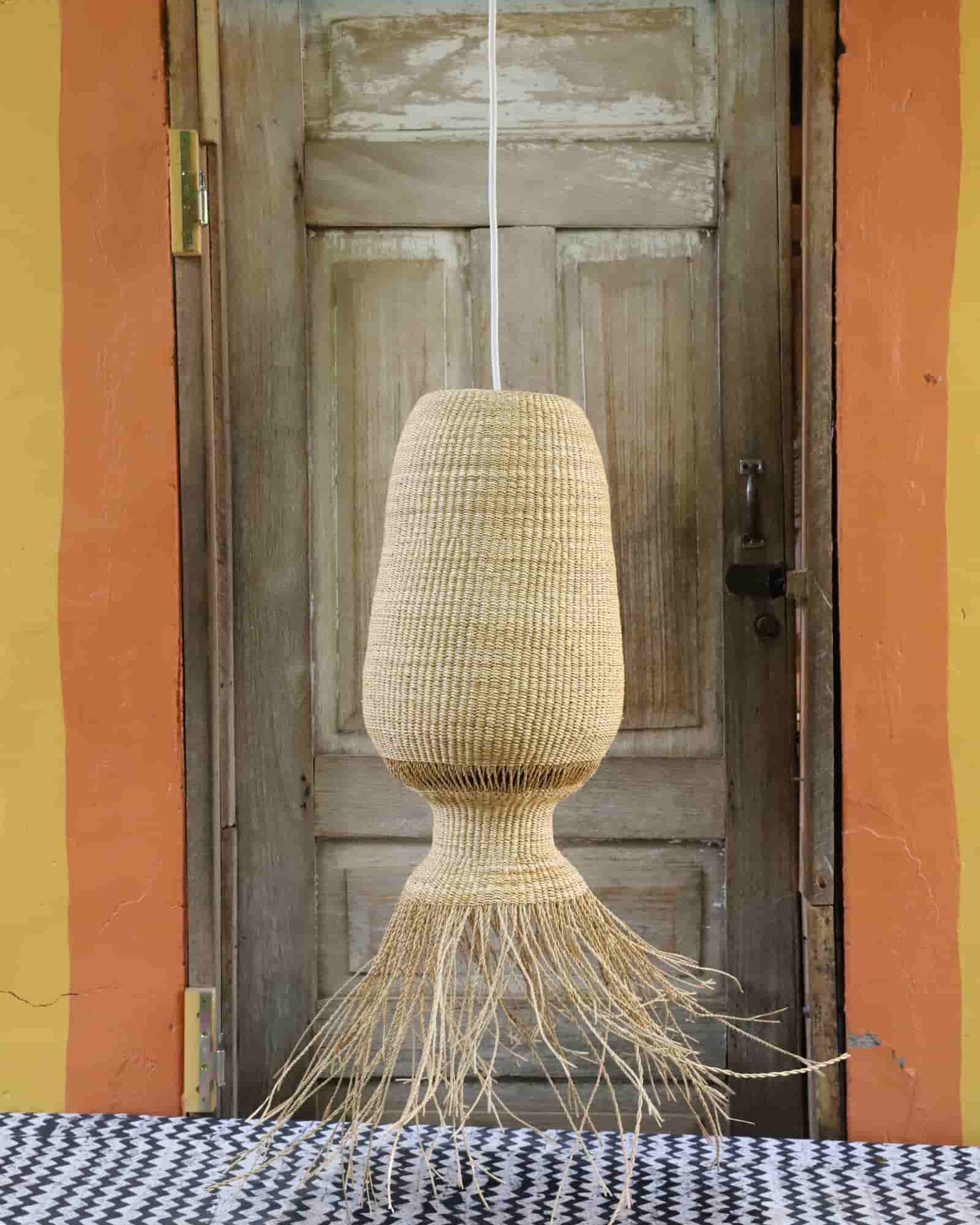Woven lamp hanging in front of a wooden door with colorful walls.