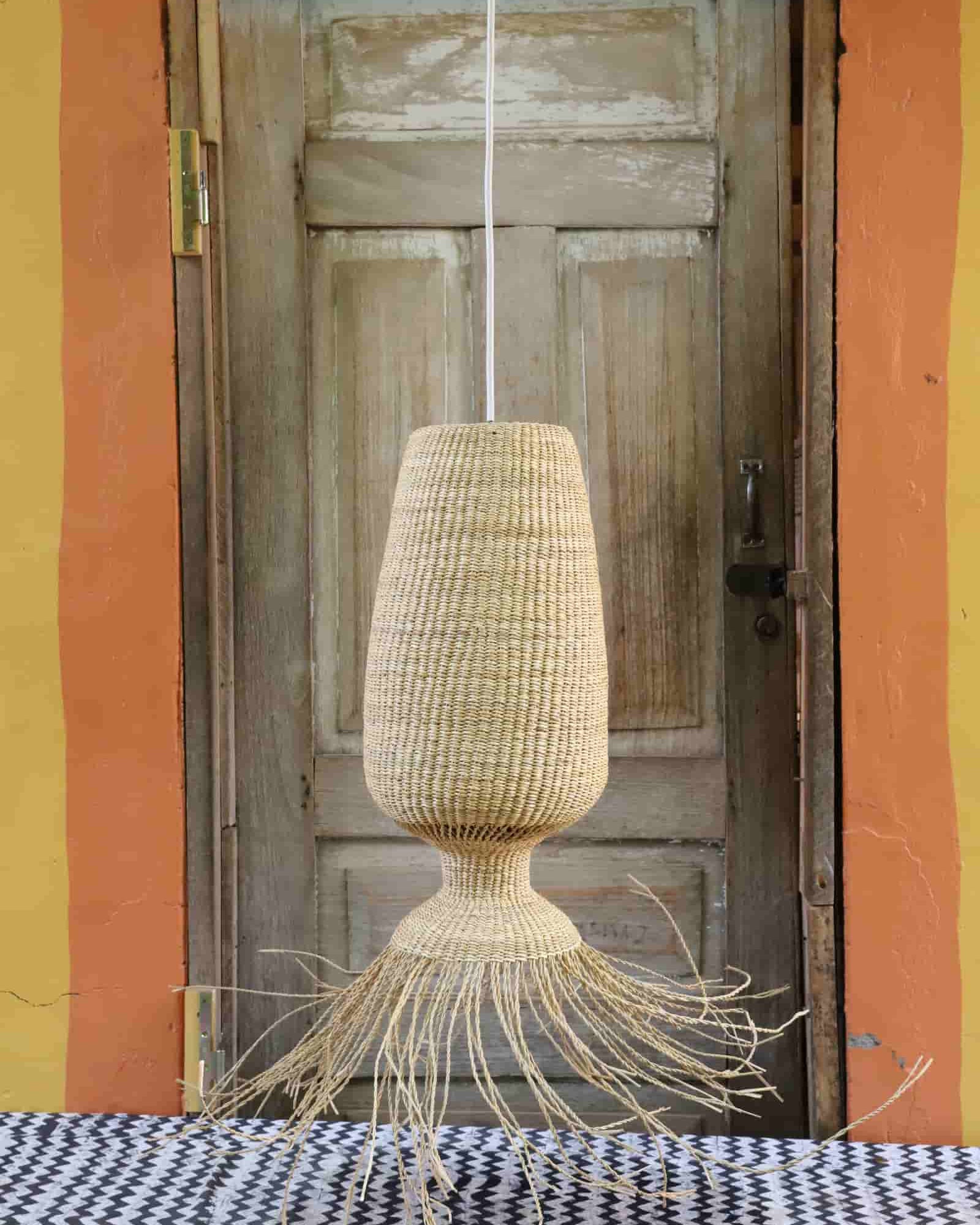 Woven lamp hanging in front of a wooden door with a colorful wall background