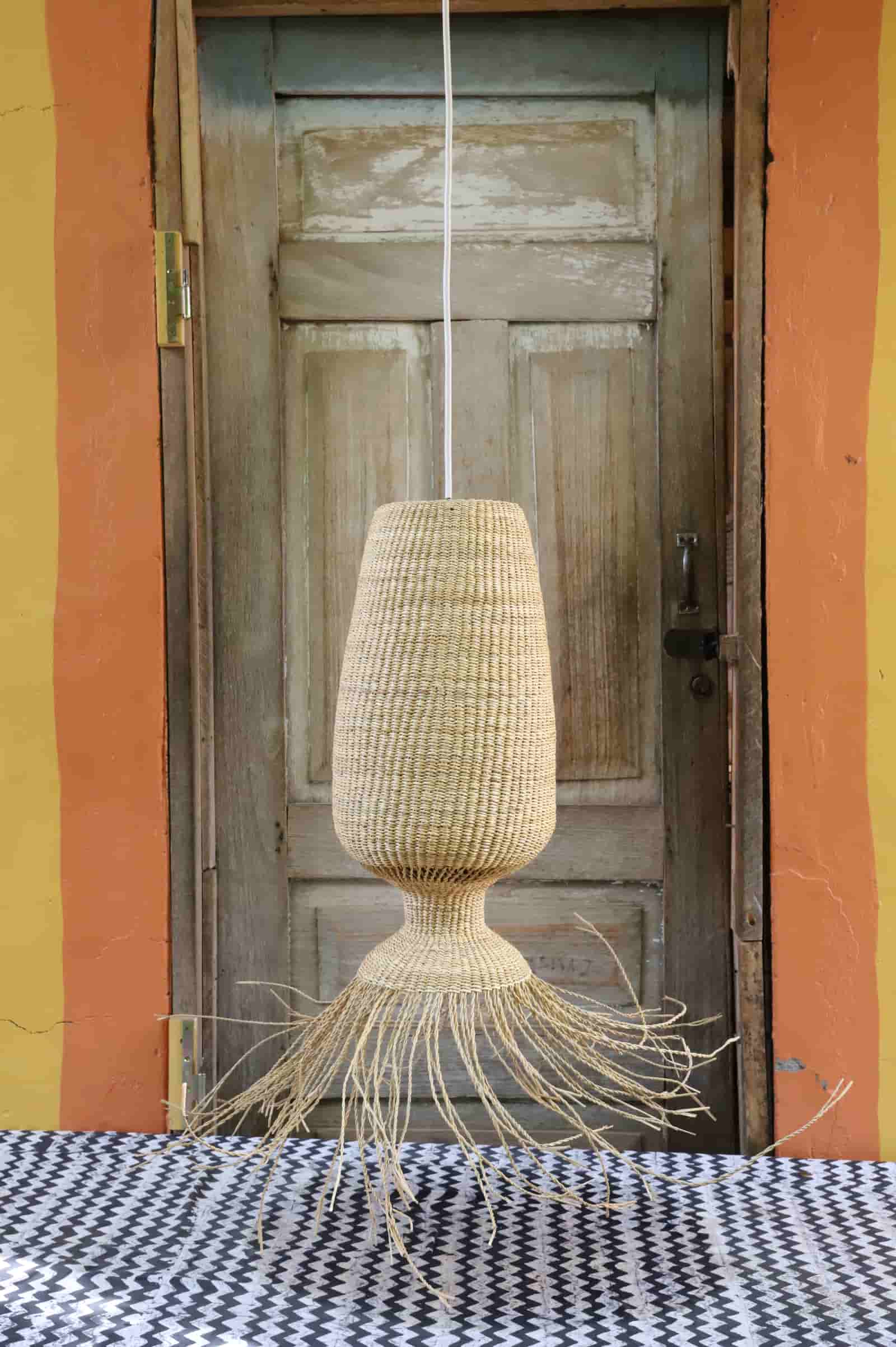 Woven lamp hanging in front of a wooden door with a colorful wall background