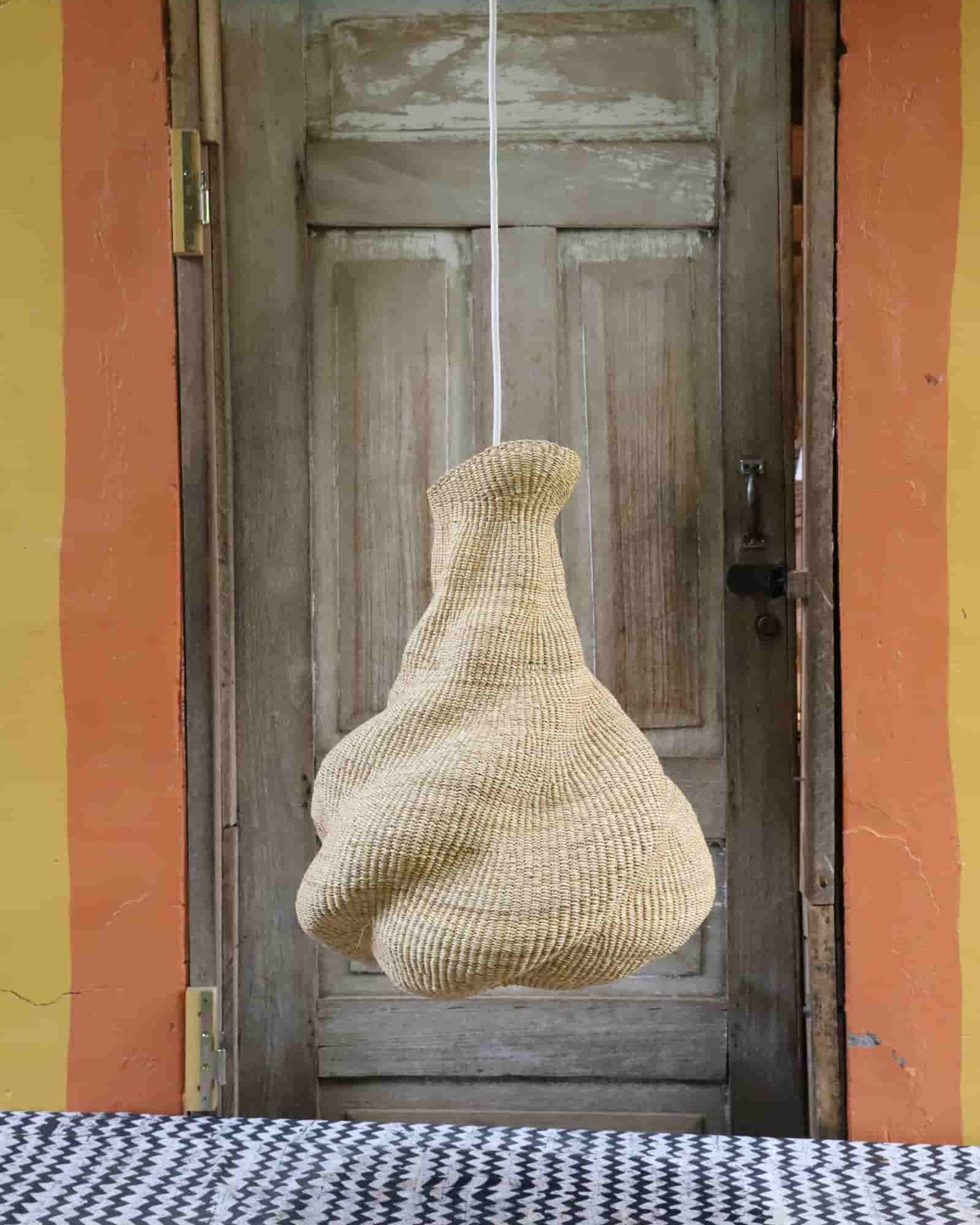 Woven basket hanging from a string in front of an open door with a colorful wall.