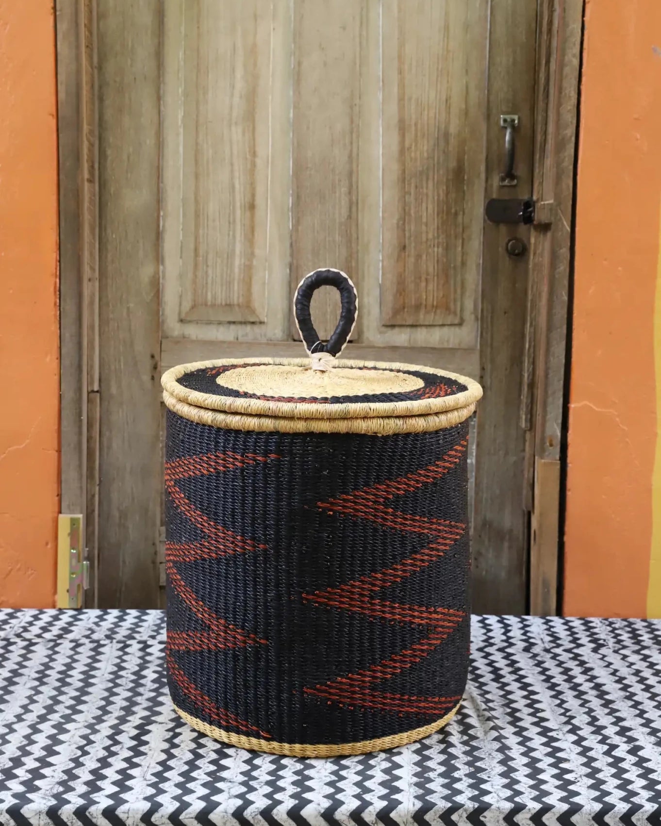 Woven basket with a lid on a table in front of a wooden door.