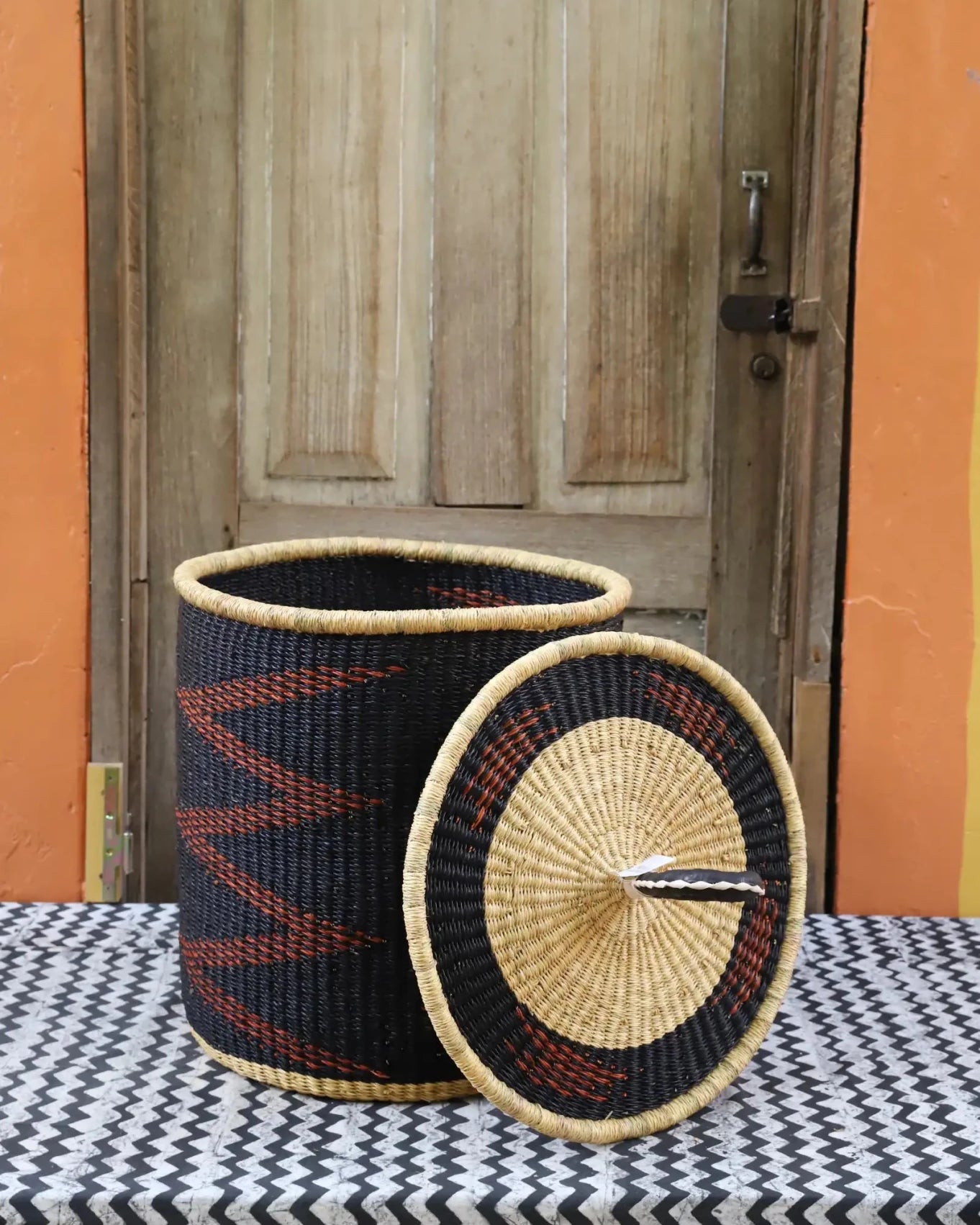 Woven baskets with black, red, and beige patterns on a table with a wooden door in the background.