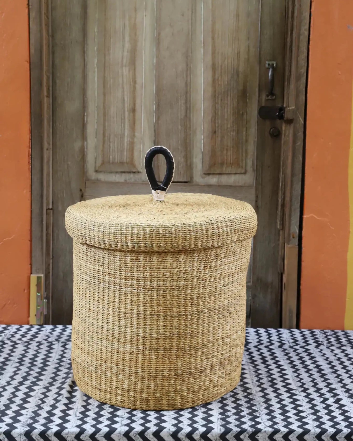 Lidded Laundry Basket (Medium) by The Baba Tree. Handwoven elephant grass with leather handle. Premium Bolgatanga artisan decor.
