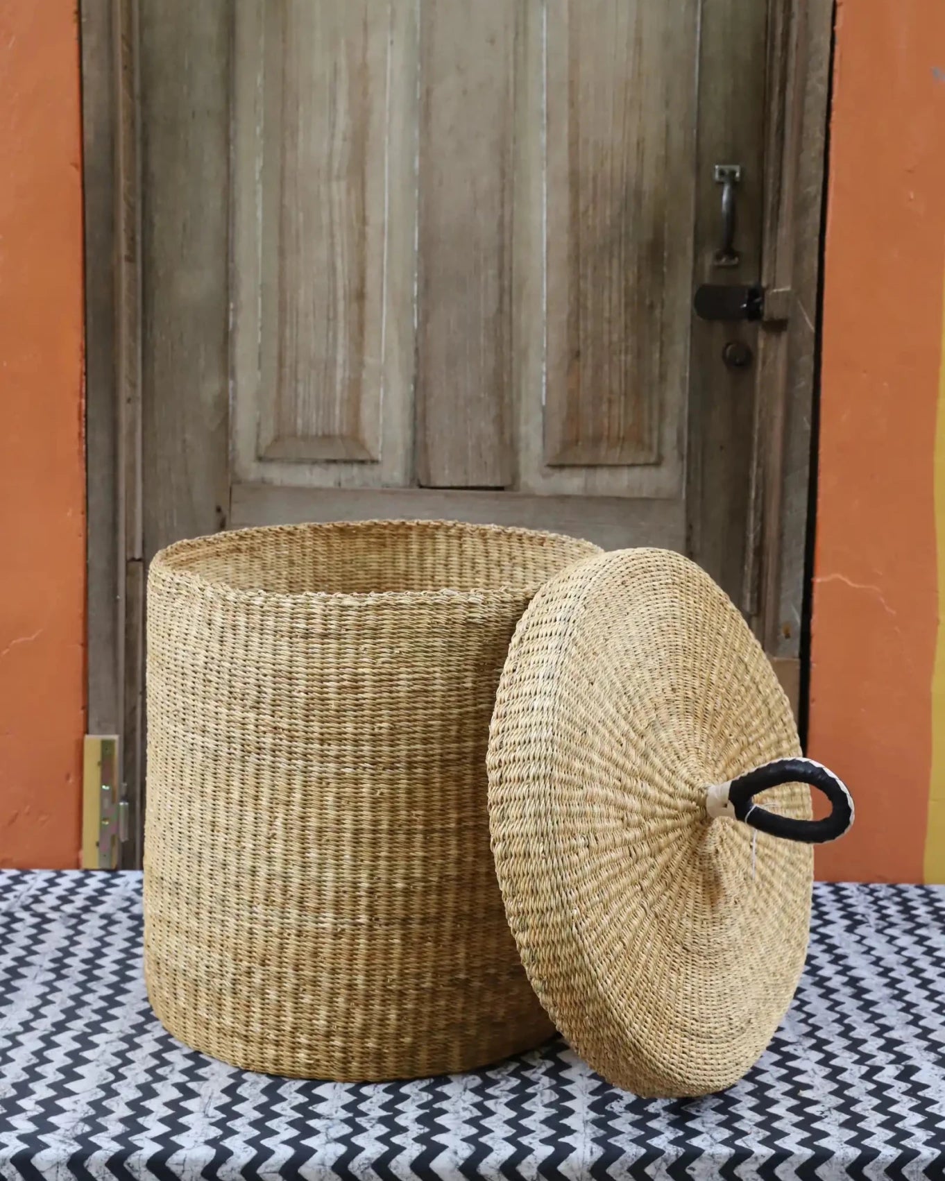 Lidded Laundry Basket (Medium) by The Baba Tree. Handwoven elephant grass with leather handle. Premium Bolgatanga artisan decor.