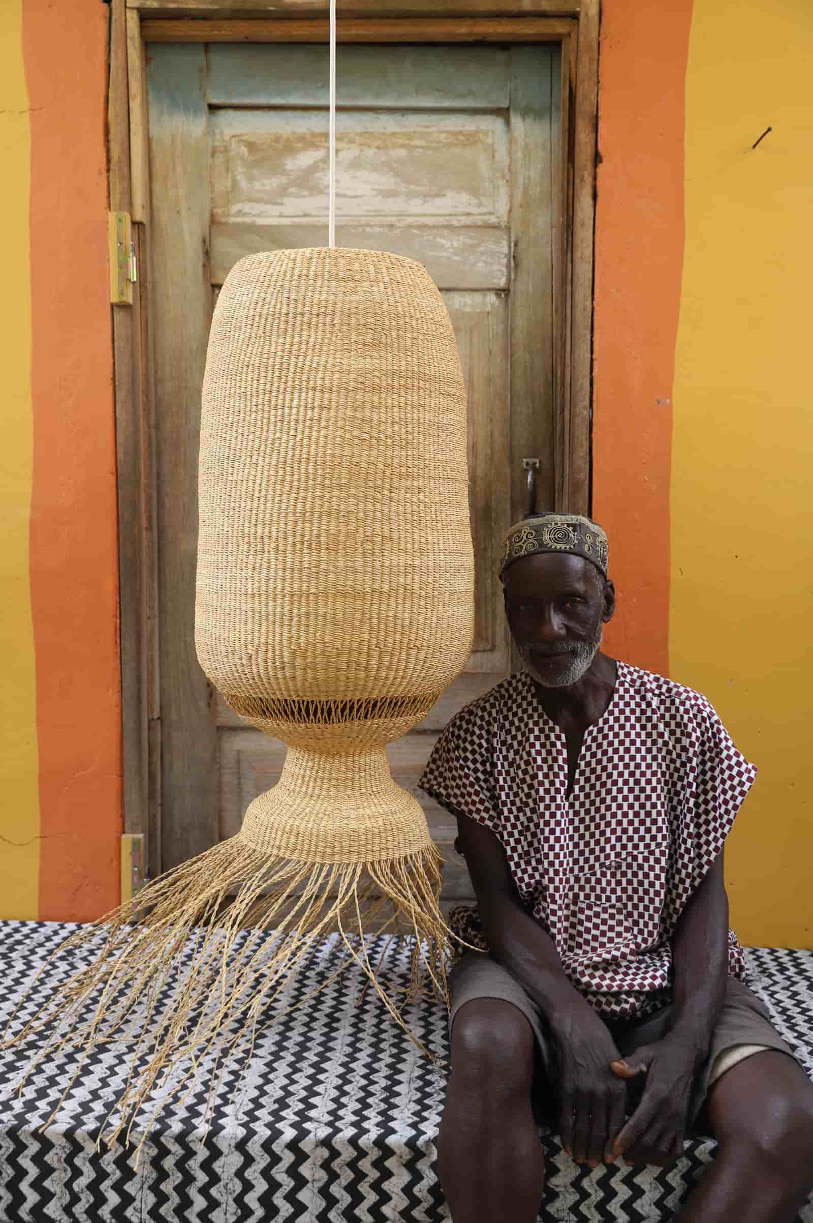 Person sitting next to a large woven lamp against a colorful wall.
