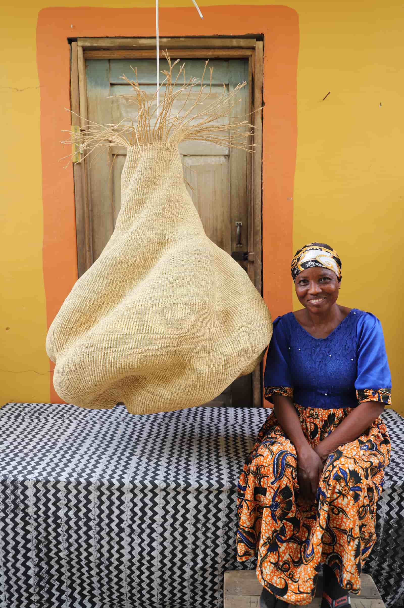 Woman sitting on a black and white cloth with a large woven basket in front of a yellow wall.