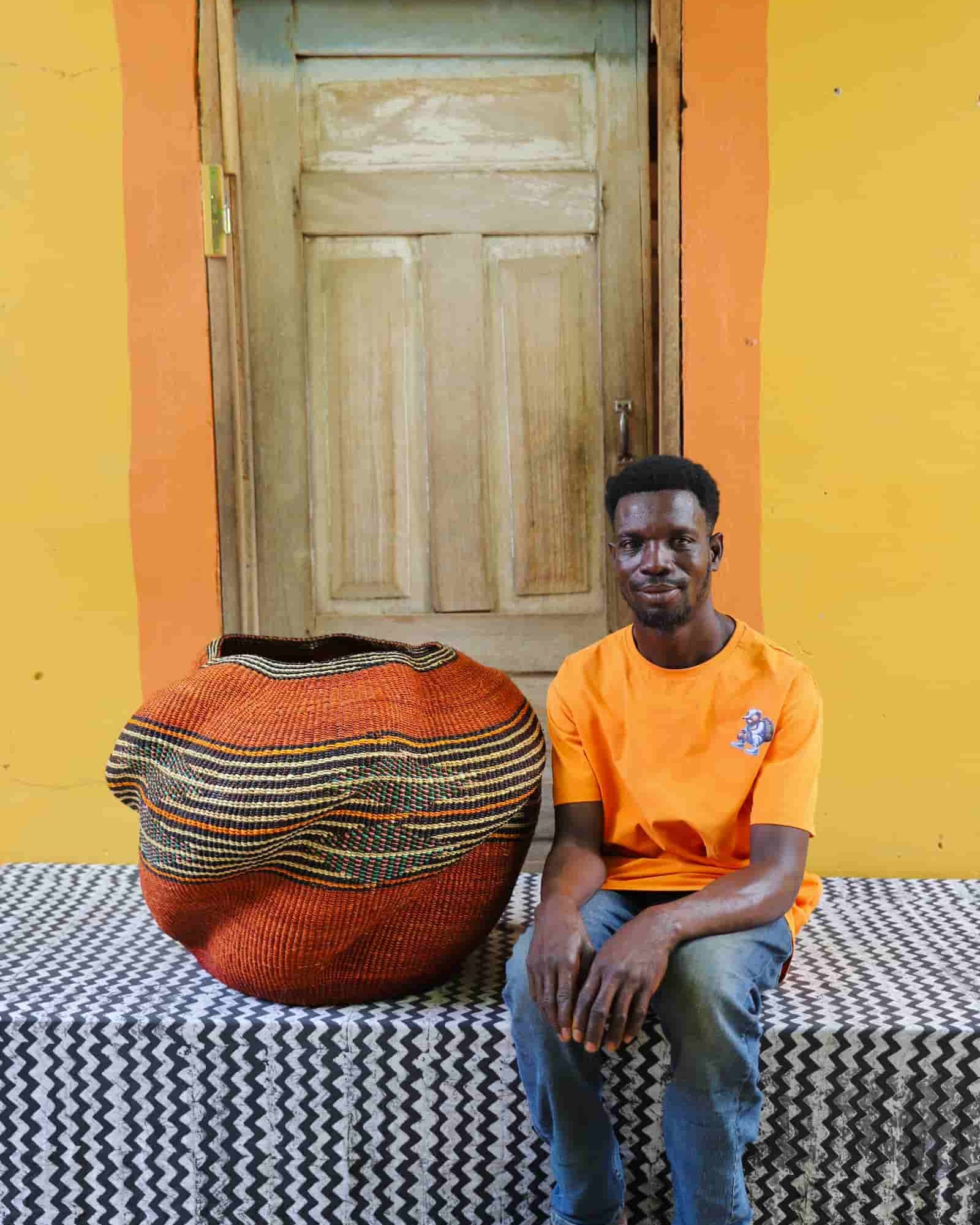 Person sitting on a patterned bench with a colorful woven basket against an orange wall.