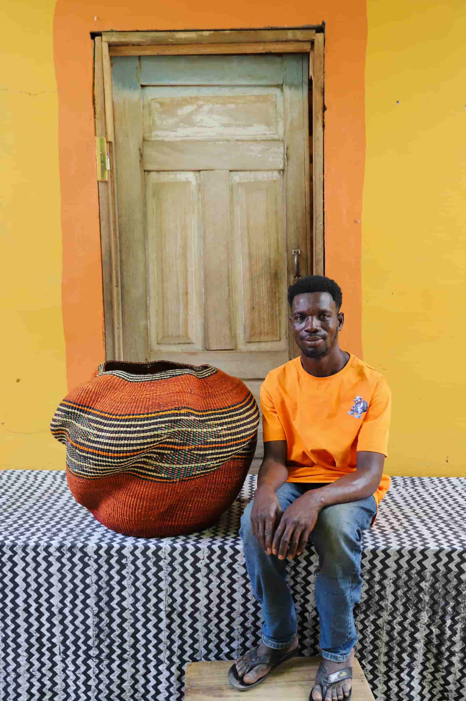 Person sitting on a patterned bench with a colorful woven basket against an orange wall.
