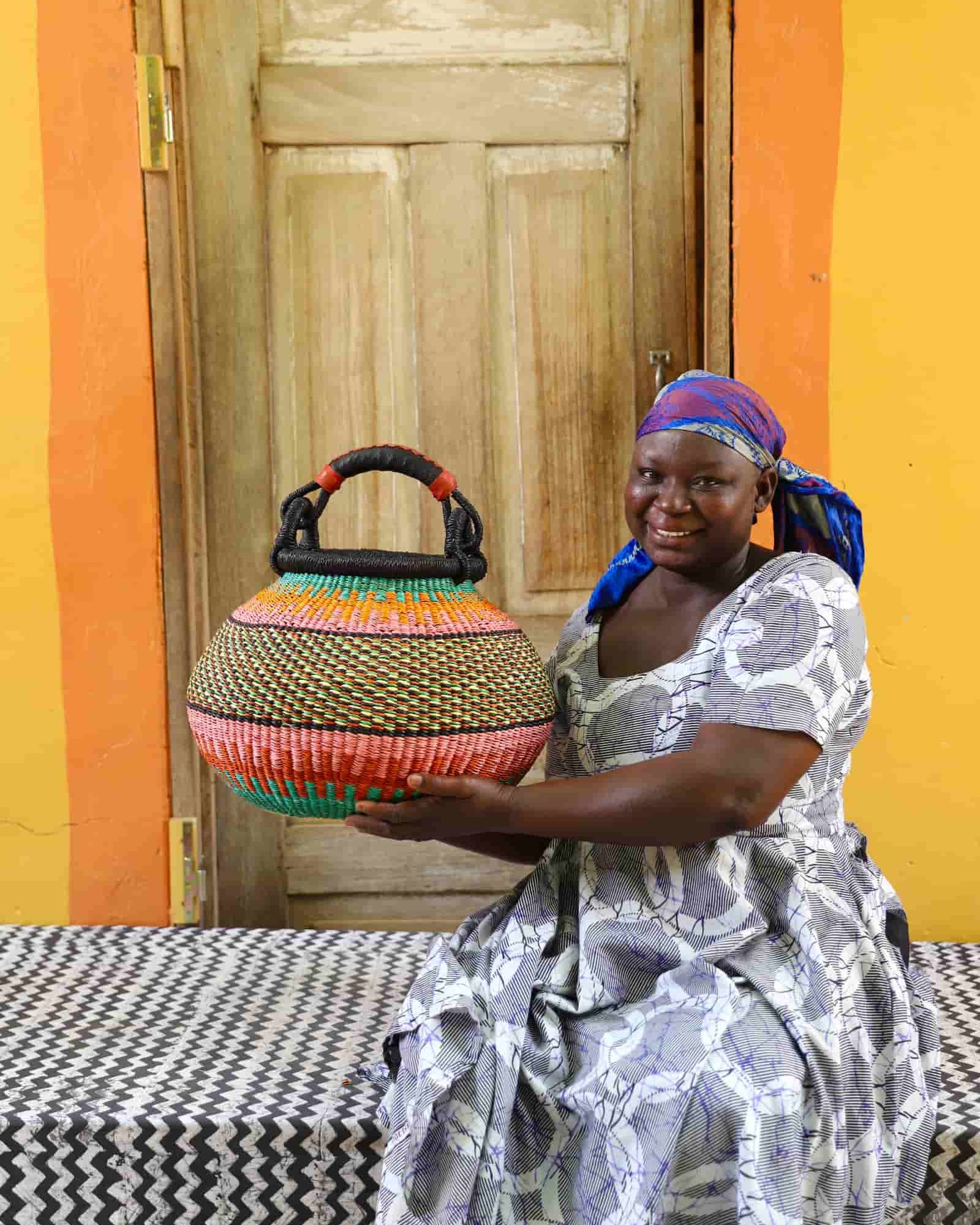 Woman holding a colorful woven basket in front of a wooden door with an orange wall.