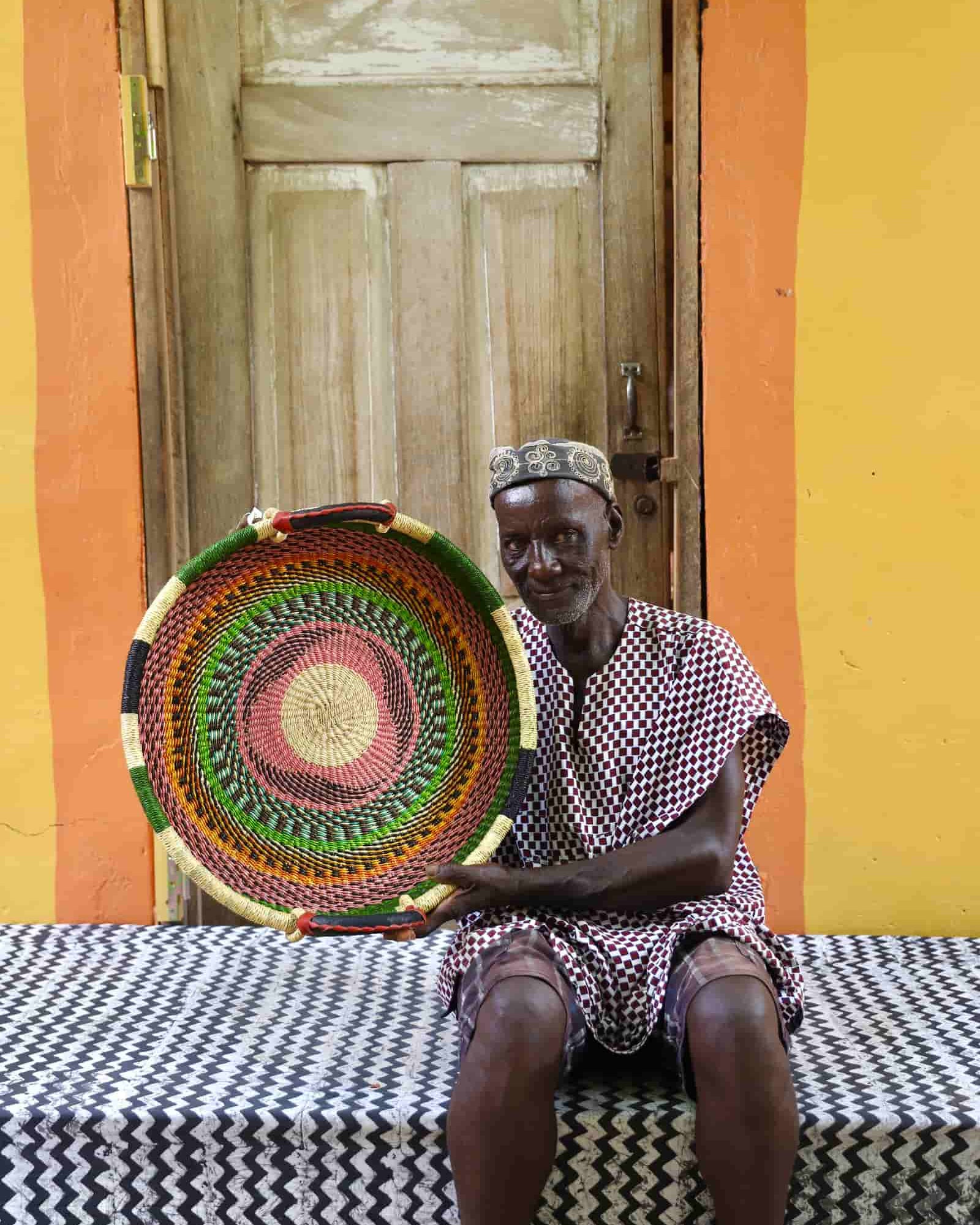 Person holding a colorful woven basket in front of a wooden door with a yellow wall.