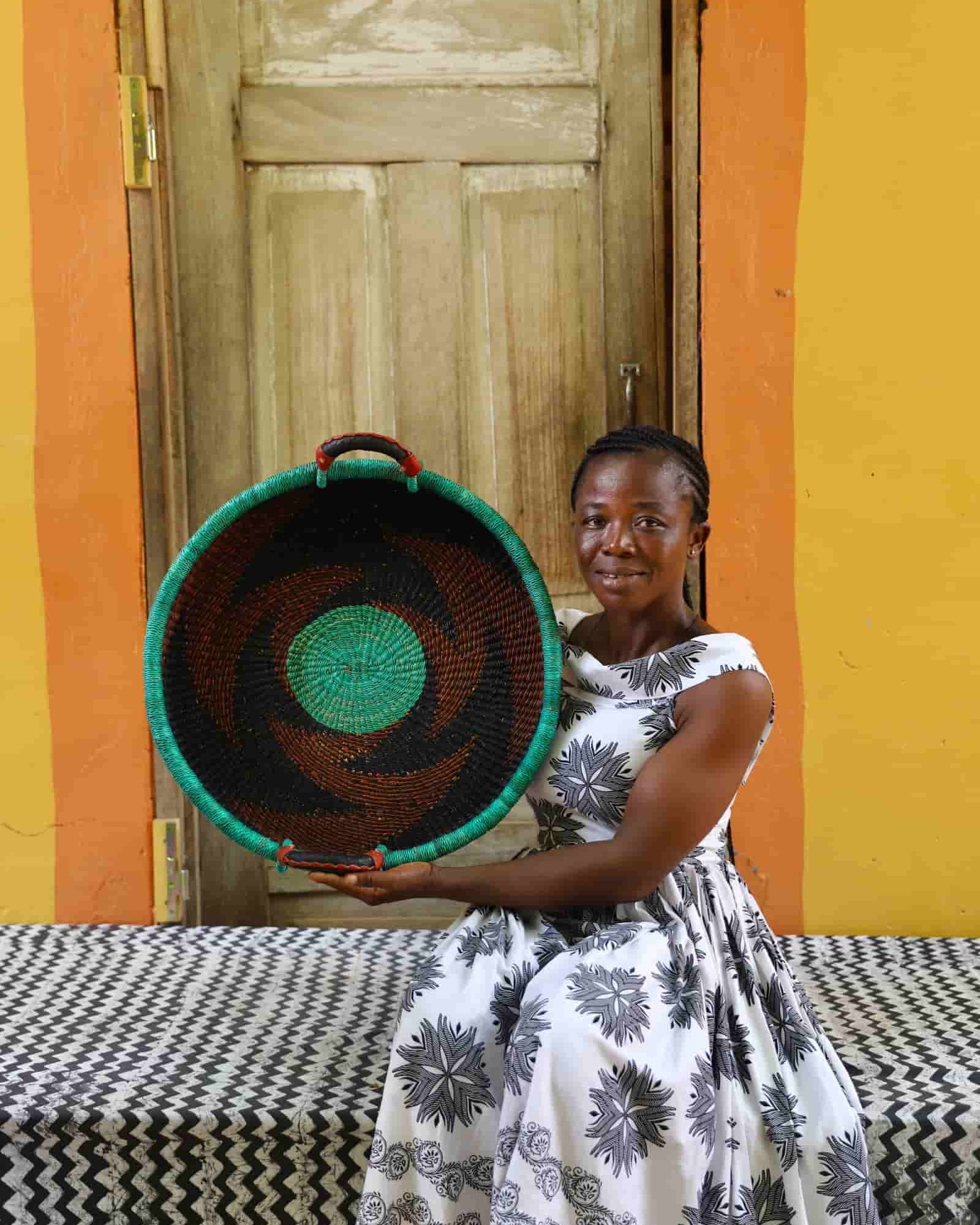 Woman holding a woven basket in front of a colorful wall and wooden door.