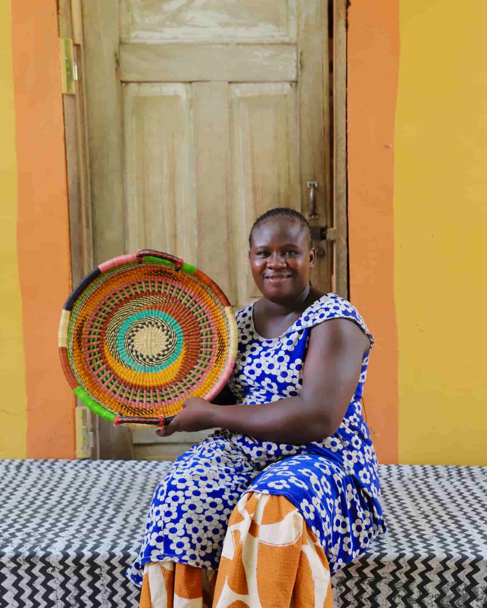 Woman holding a colorful woven basket in front of a yellow wall.