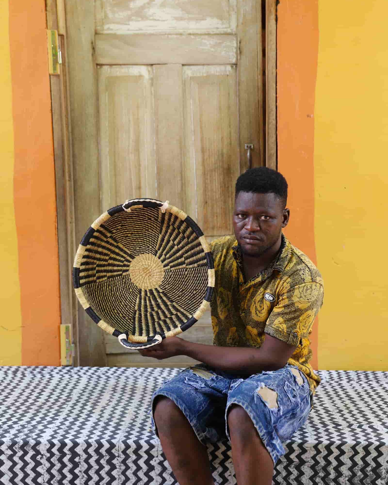 Man holding a woven basket in front of a colorful wall with a wooden door.