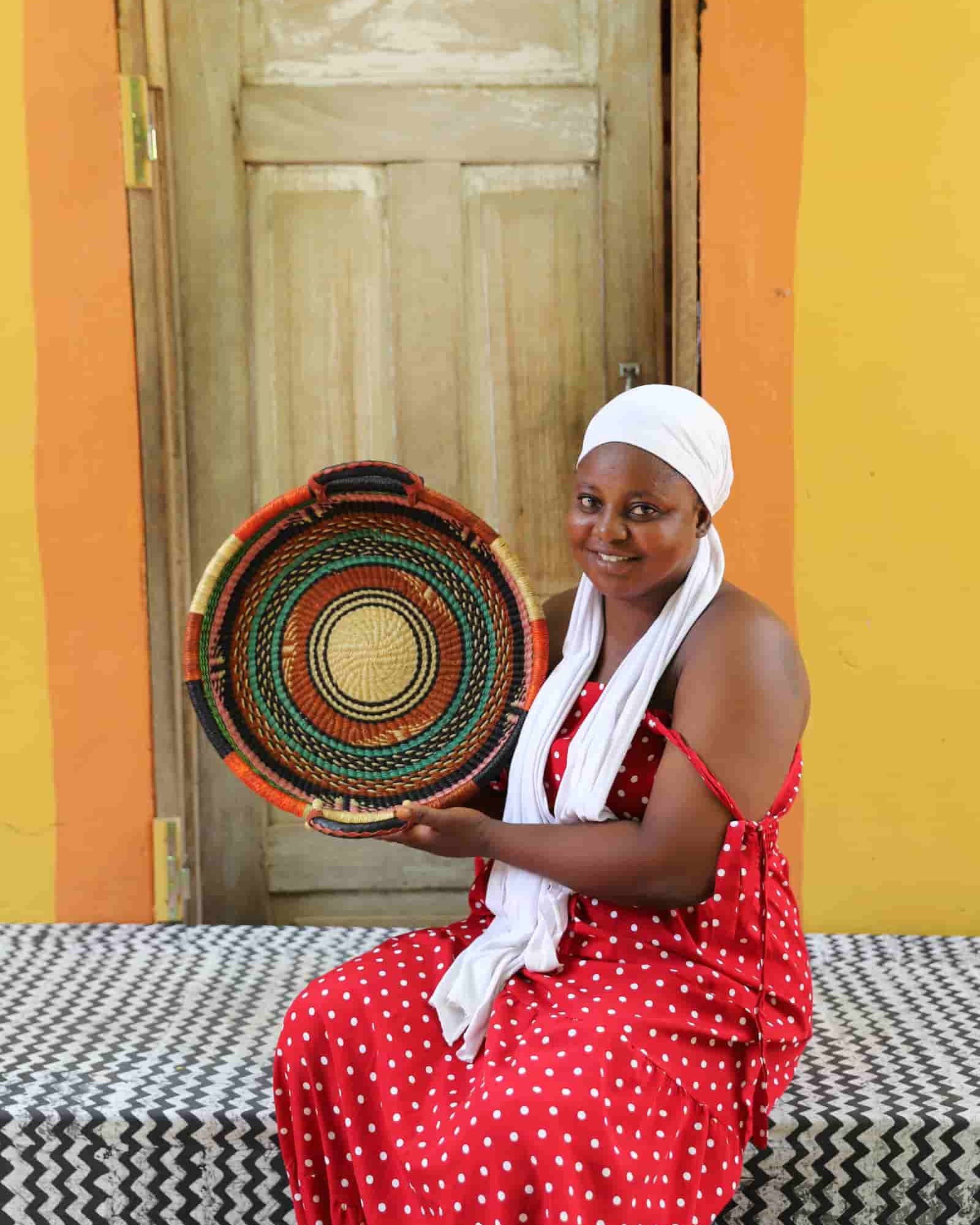 Woman in a red dress holding a colorful woven basket against a yellow wall.