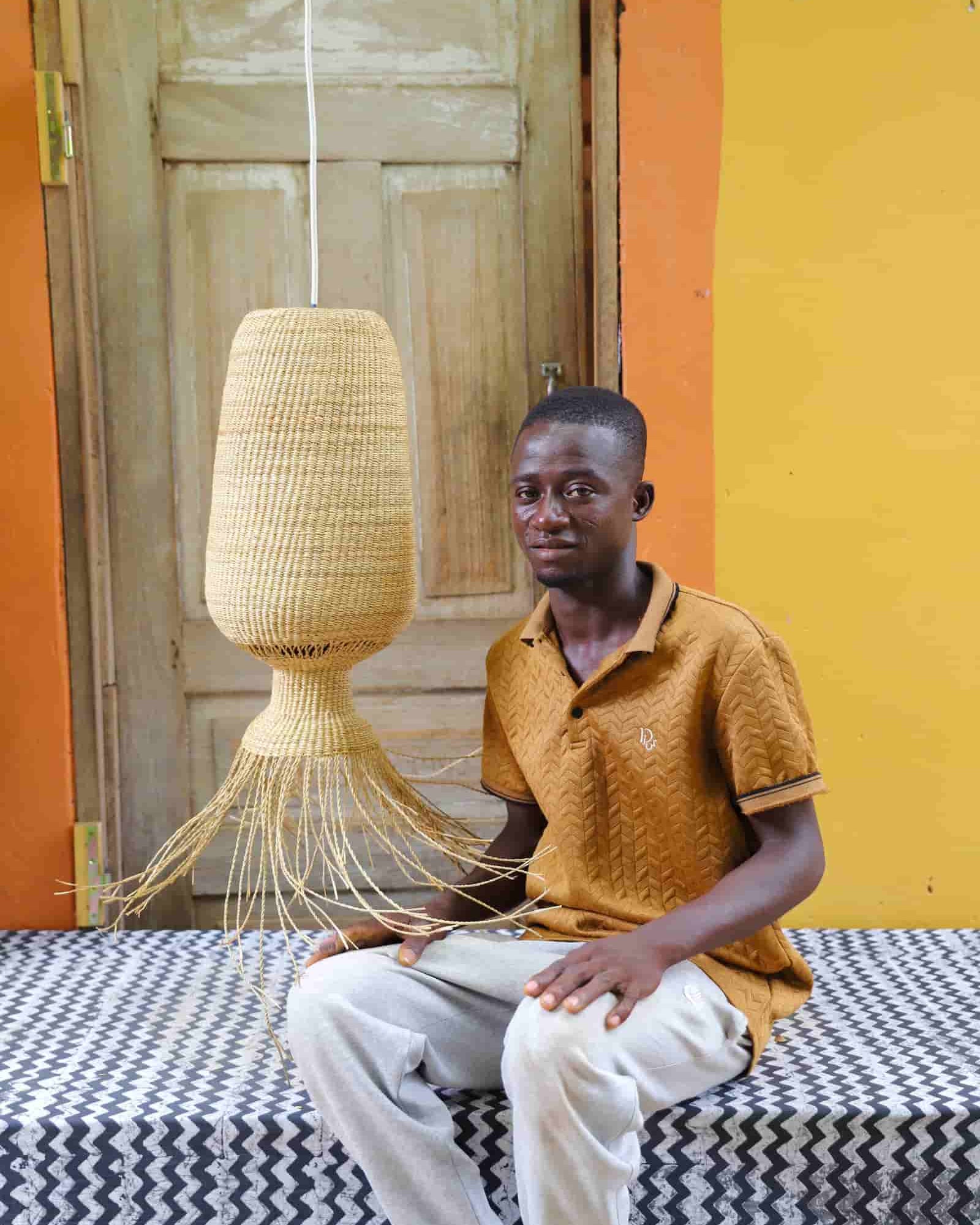 Man sitting on a bed with a woven lamp in a room with orange walls and a wooden door.