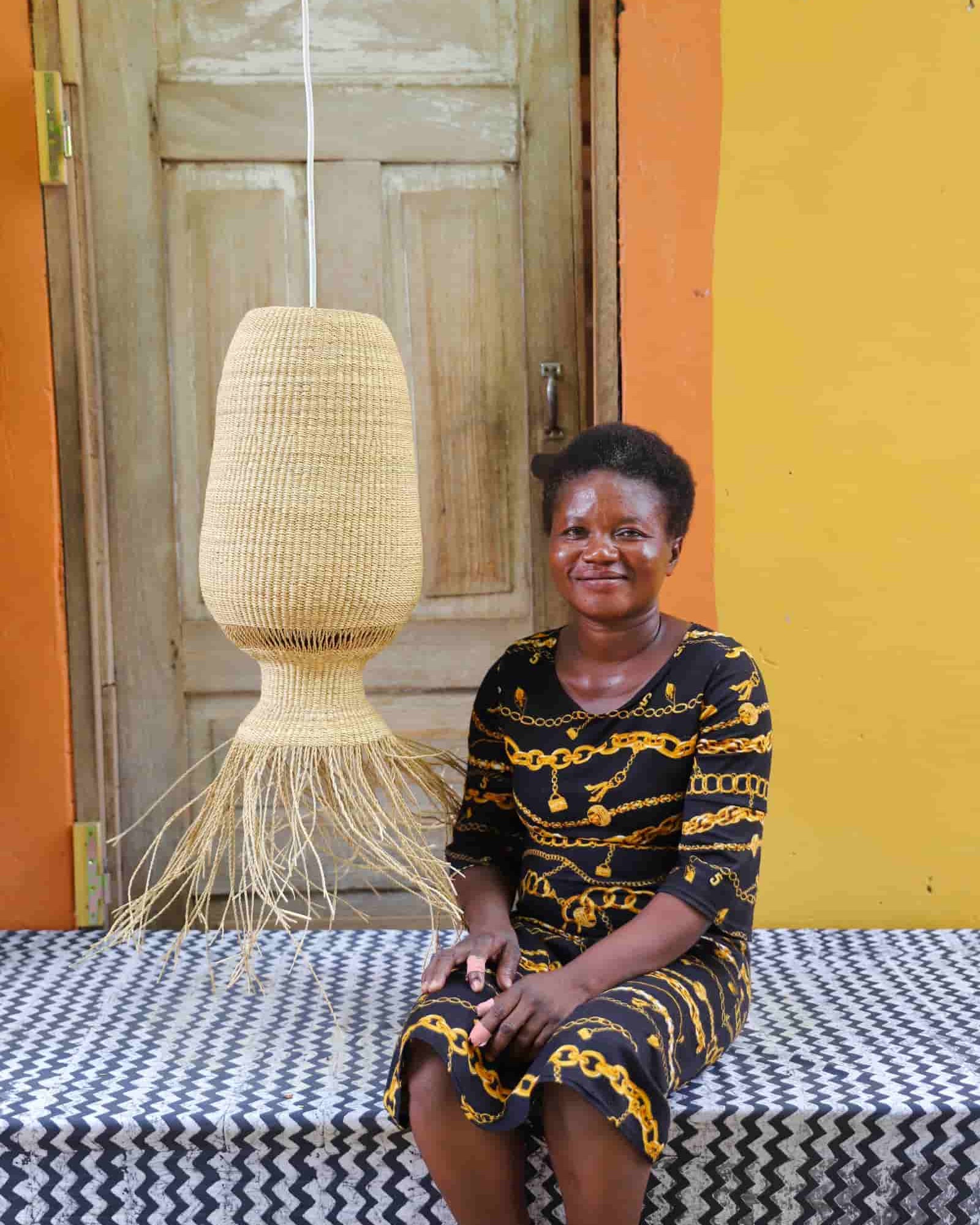 Woman sitting on a bench with a woven lamp behind her against a colorful wall.