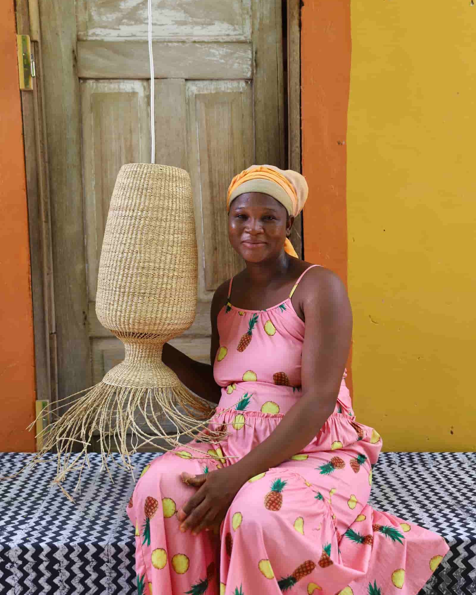Woman in a pink dress with pineapple pattern holding a woven lampshade against a colorful background.