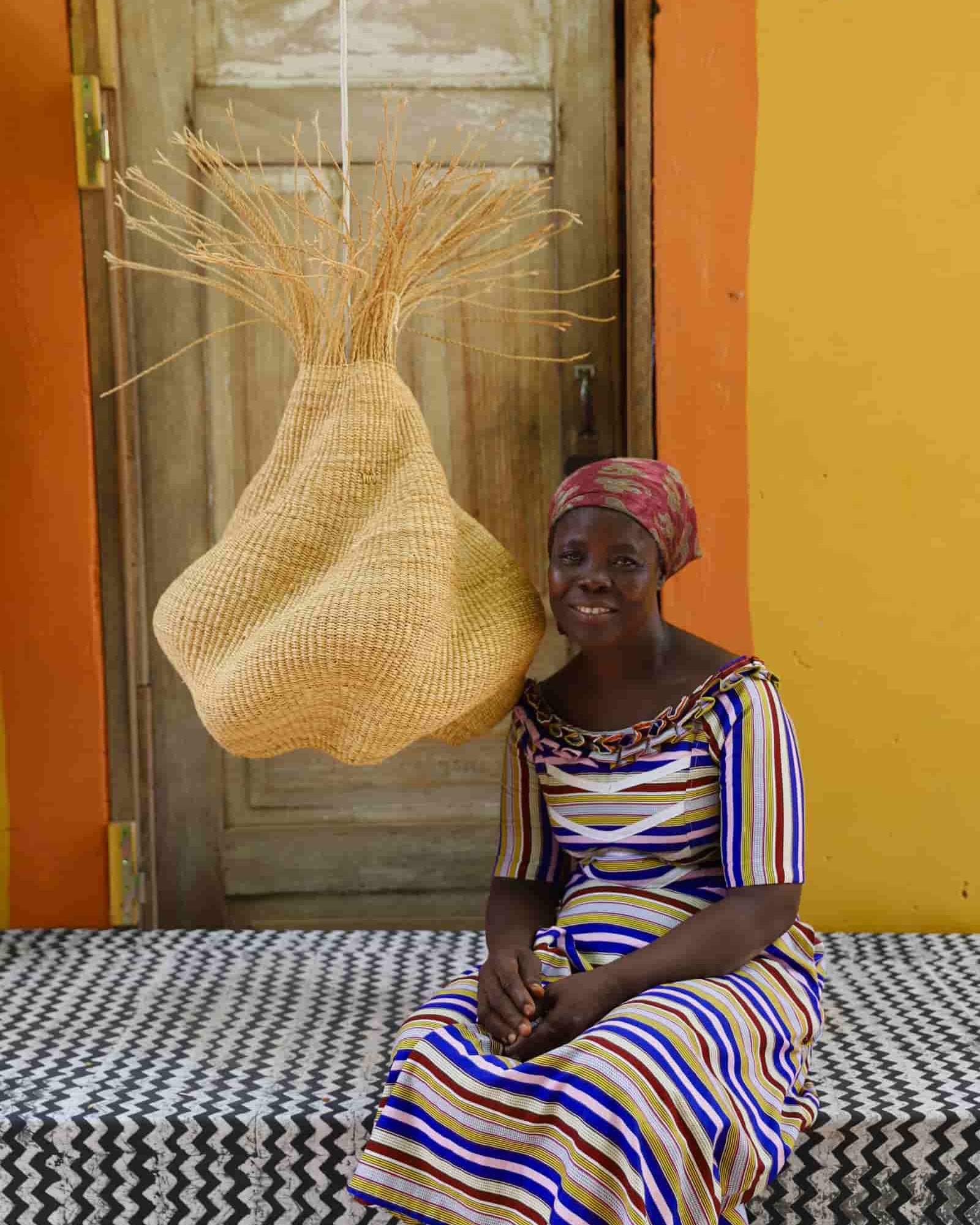 Woman sitting on a bed with a woven basket against a colorful wall.